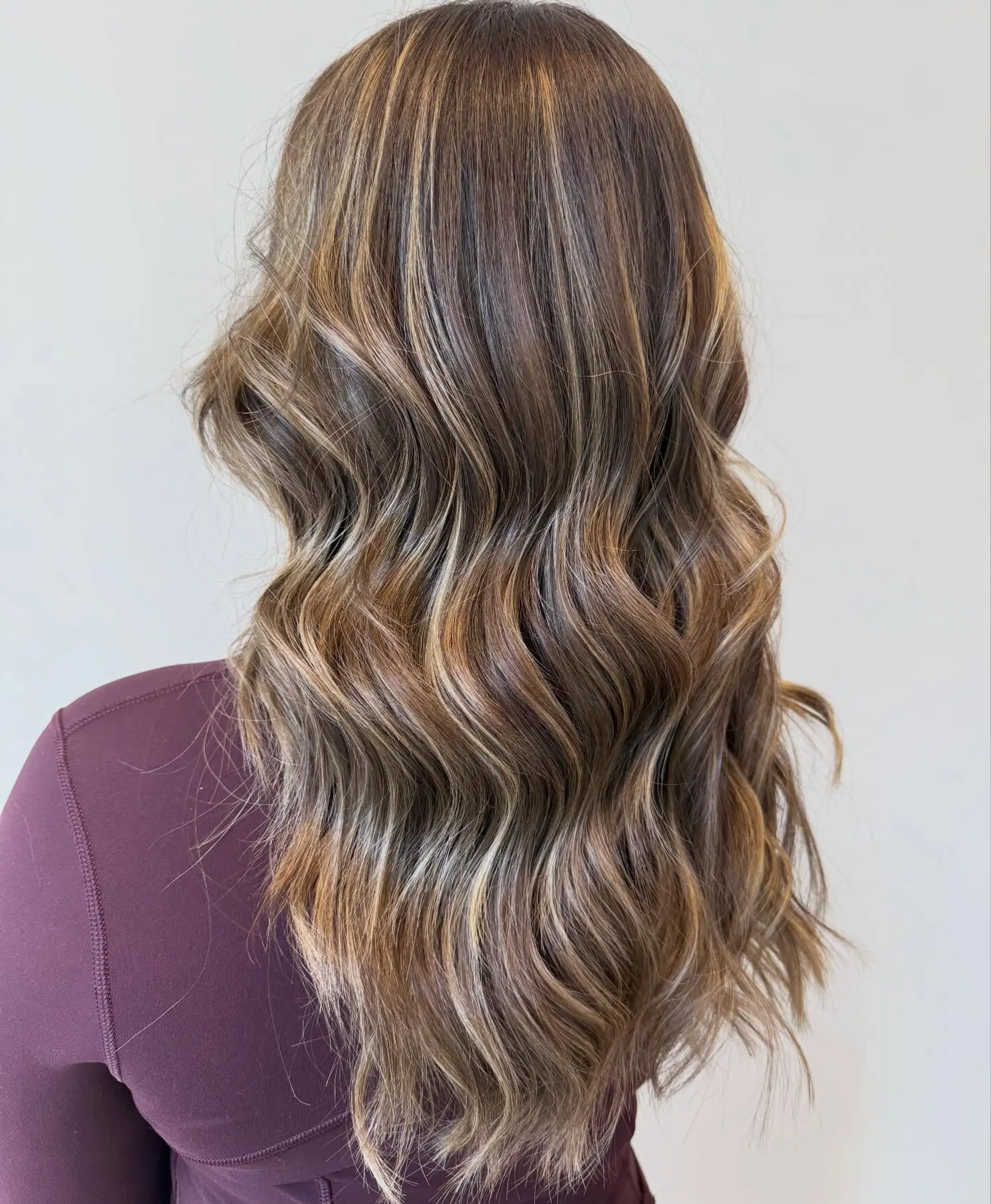 Long brown hair with soft caramel and honey blonde balayage highlights, styled in loose beachy waves. 1