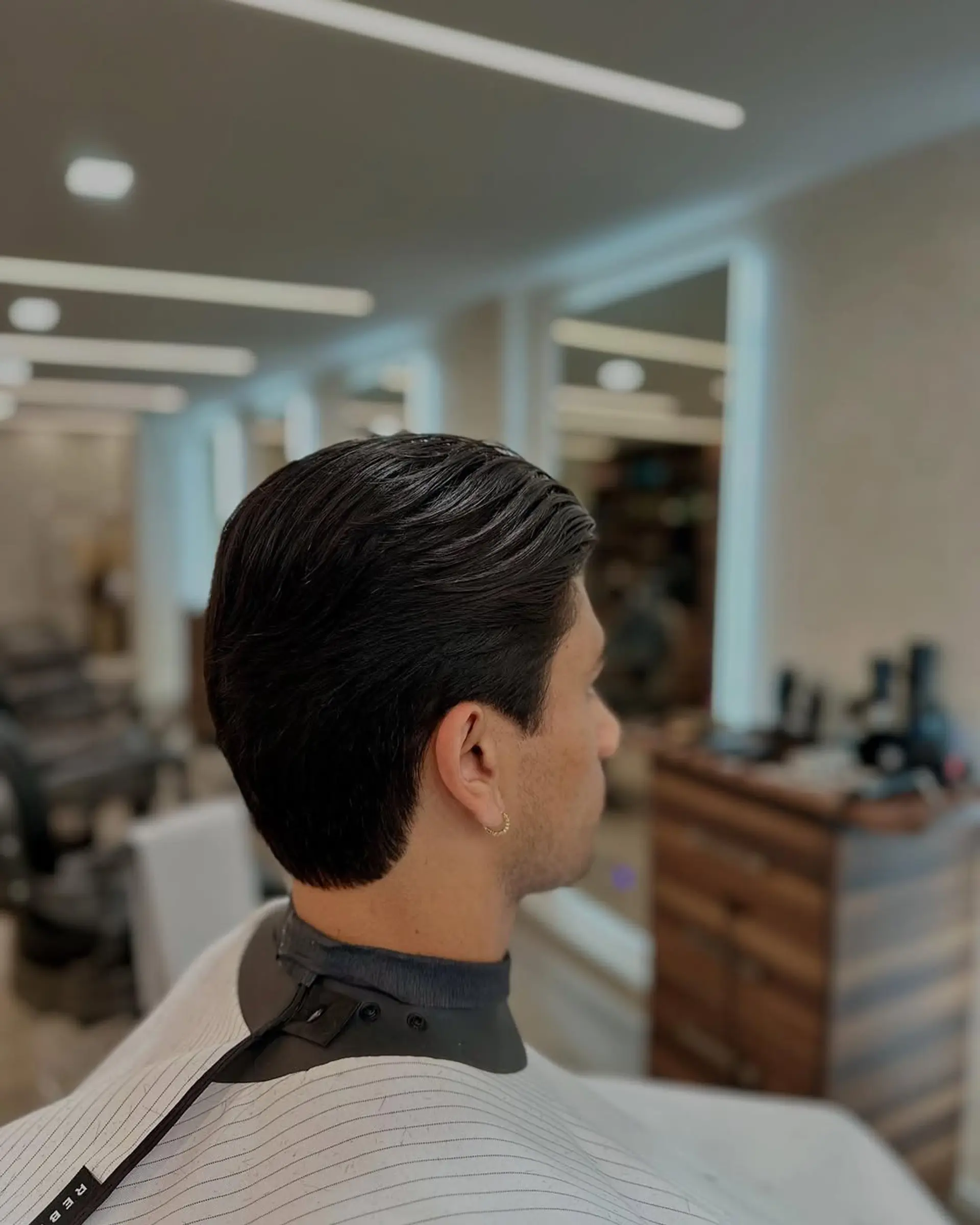 A refined men's haircut showcasing medium-length wavy hair swept back from the face, complemented by neatly tapered sides and a clean, natural neckline. 1