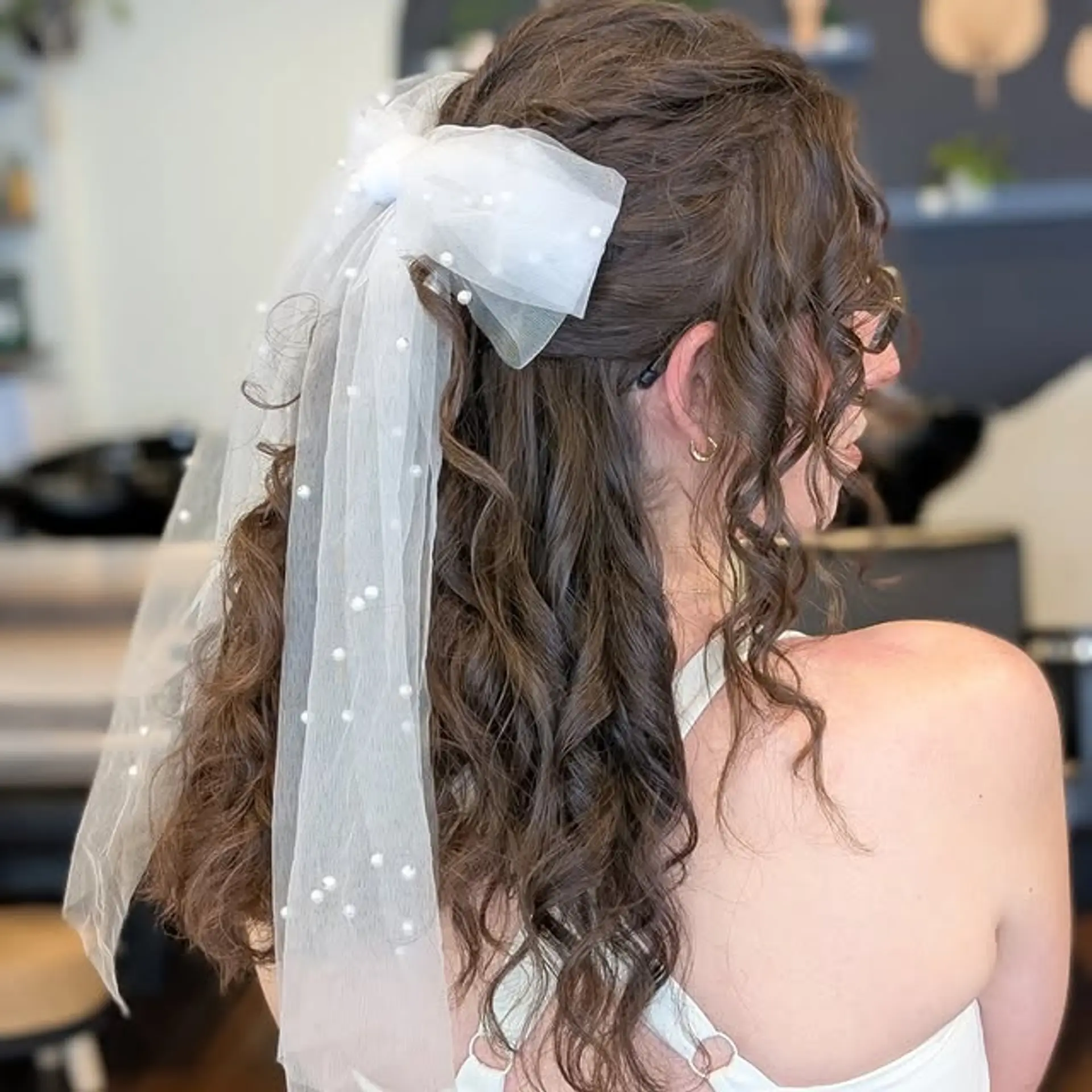 A romantic half-up half-down curly hairstyle adorned with a bow veil, perfect for a wedding or special event. 1