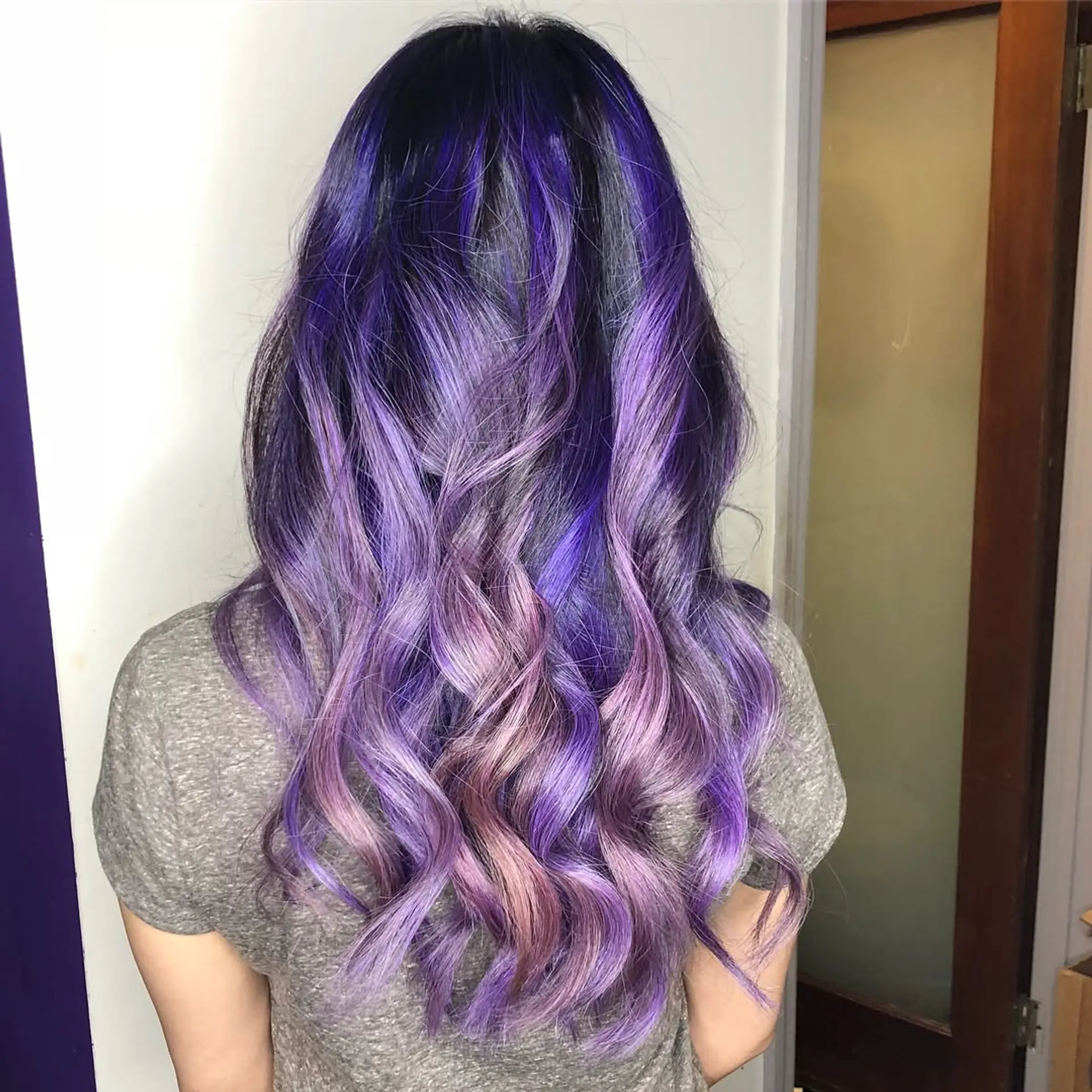 Long wavy hair featuring a seamless transition from deep root shadow into rich violet, indigo, and soft lavender curls. 1