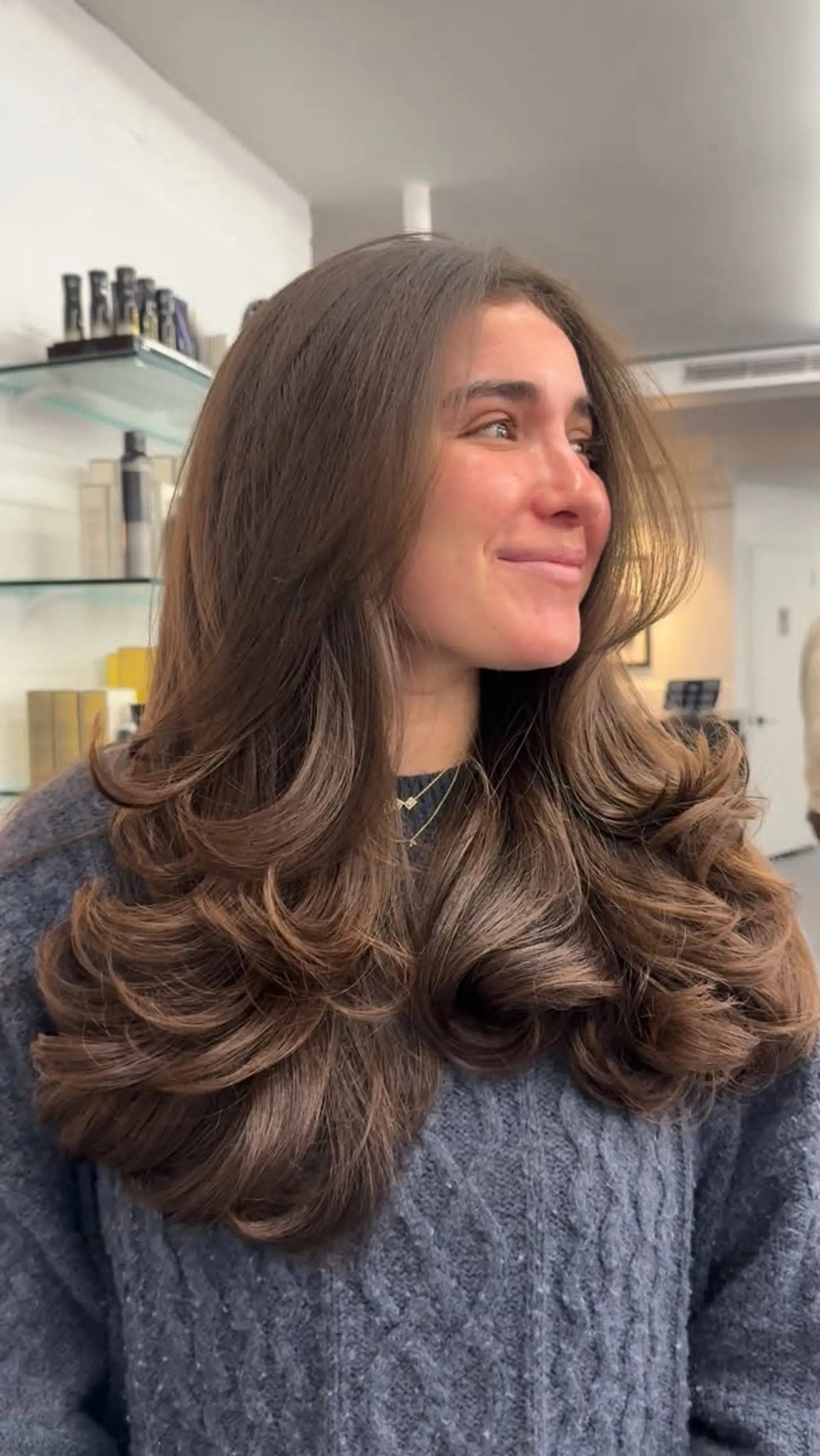 Long chocolate brown hair cut into seamless, face-framing layers and styled into a voluminous, bouncy 90s blowout with flicked-in curls. 1