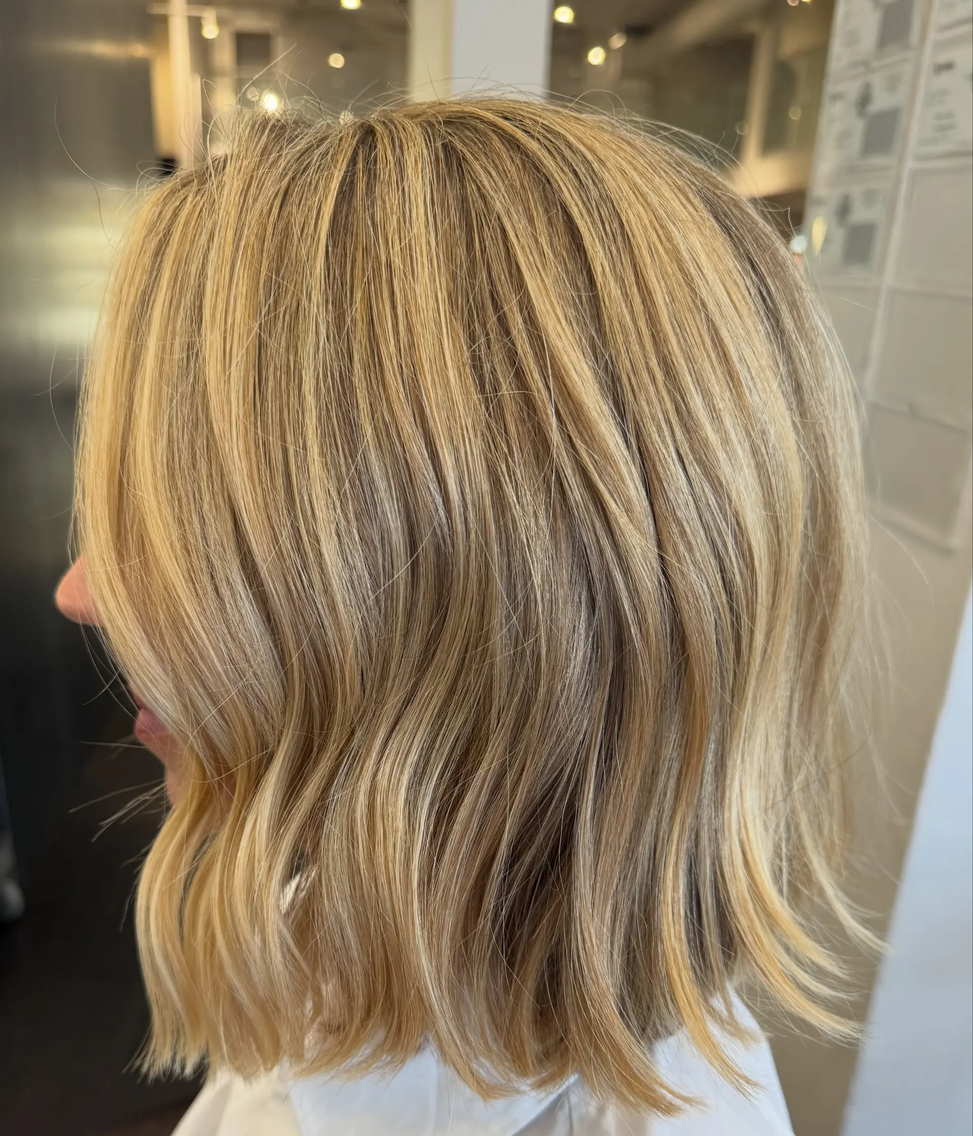 A textured, neck-length bob styled with soft, subtle waves in multi-dimensional warm buttery blonde highlights. 1