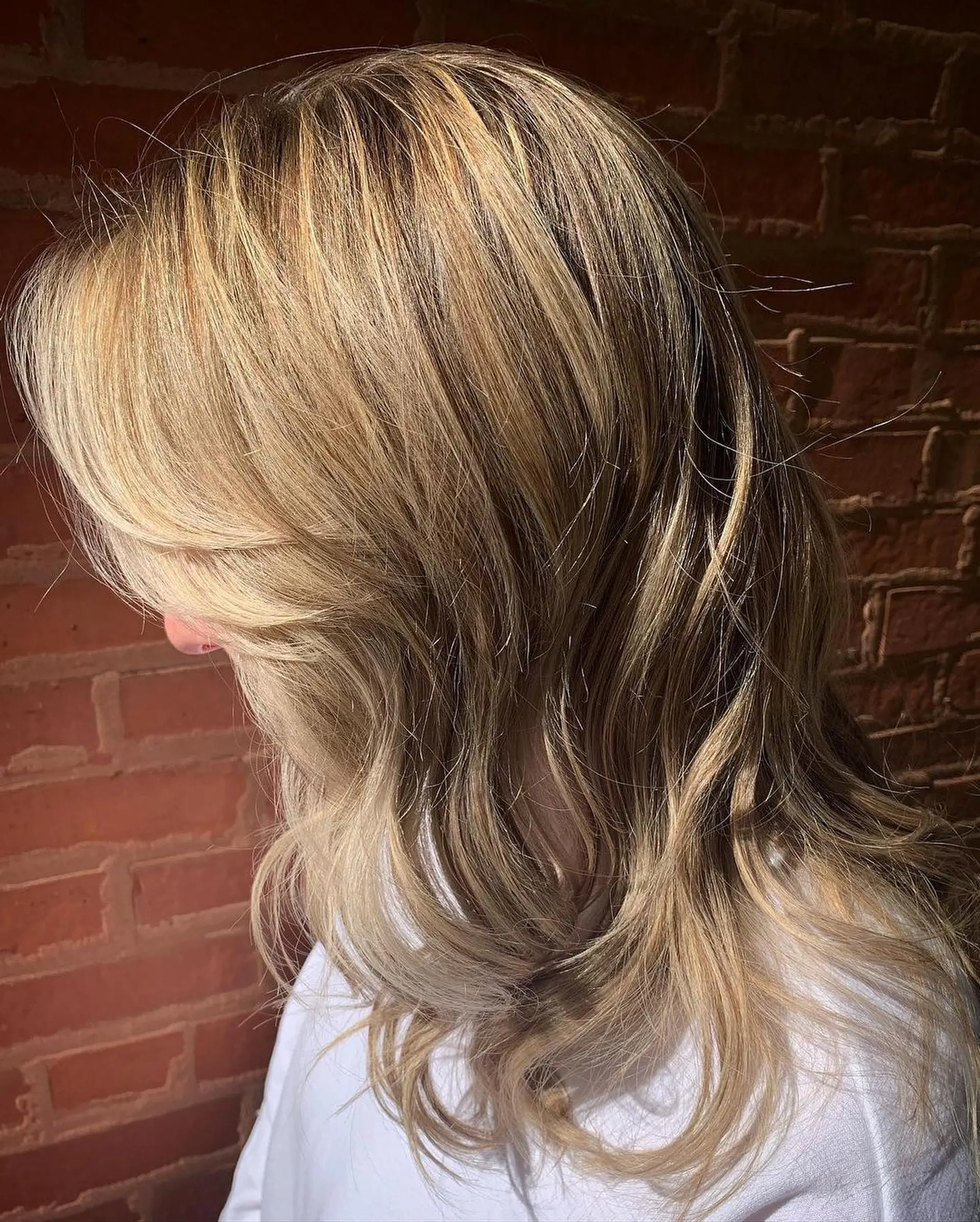 Medium-length dimensional blonde hair cut with face-framing curtain bangs and styled in loose, textured waves. 1
