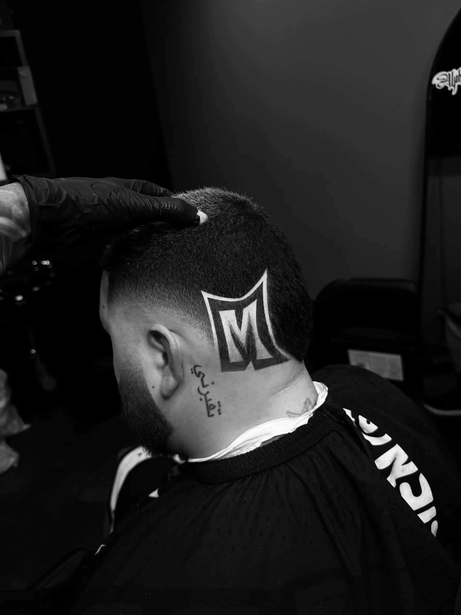 A clean fade haircut featuring a precise, shaved-in custom letter 'M' hair design on the side of the head. 1