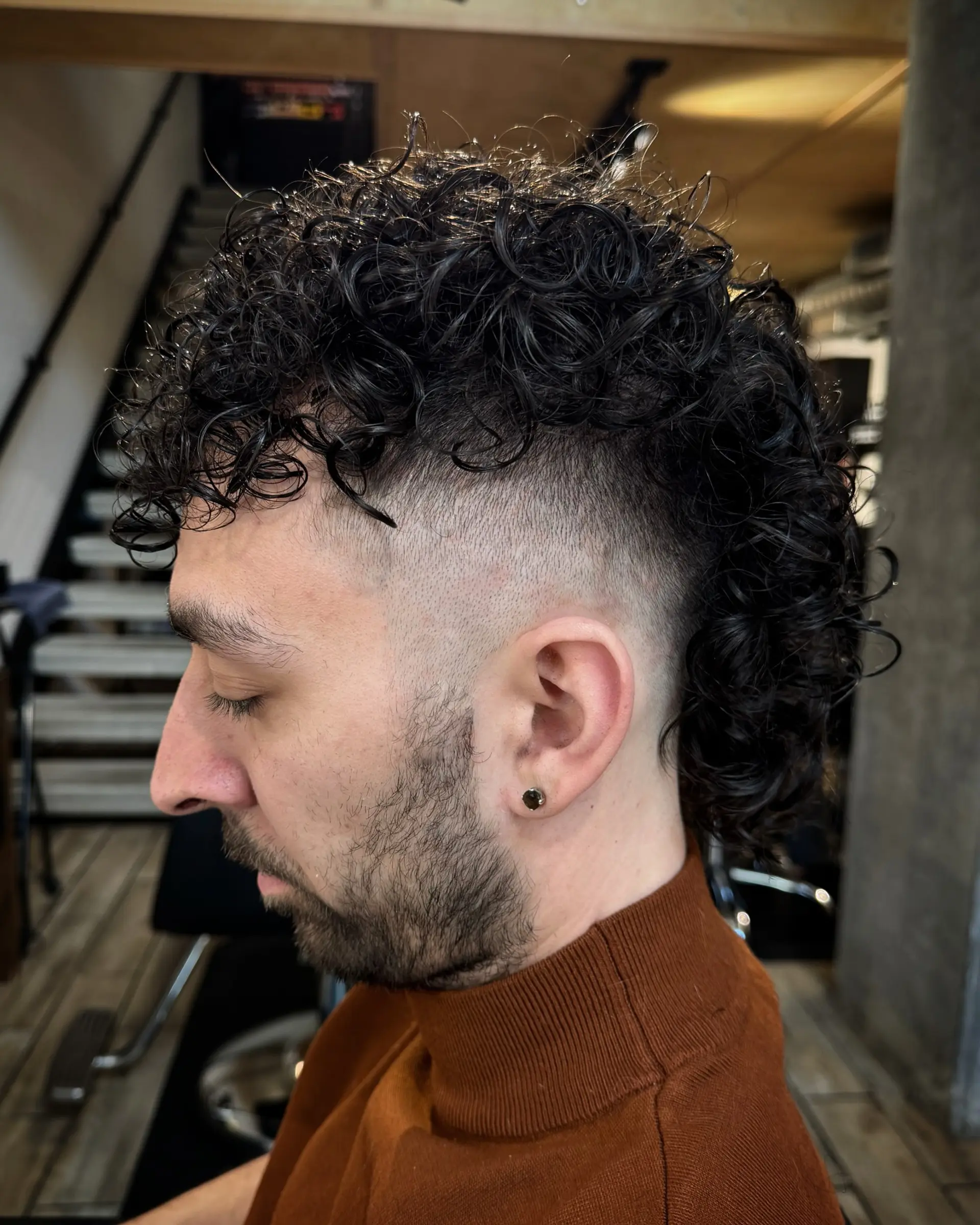 A curly mullet style featuring a clean skin fade around the sides with defined dark curls along the top and back. 1