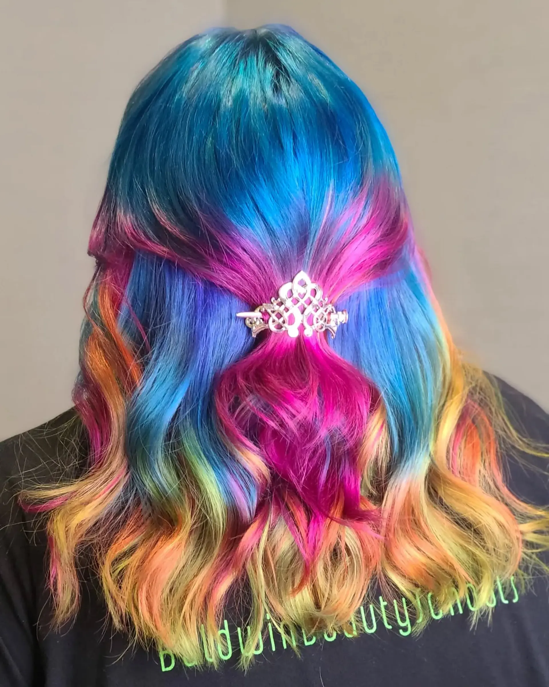Long, wavy hair dyed in a striking rainbow palette of blues, pinks, purples, oranges, yellows, and greens, styled in a half-up twist secured with a decorative clip. 1