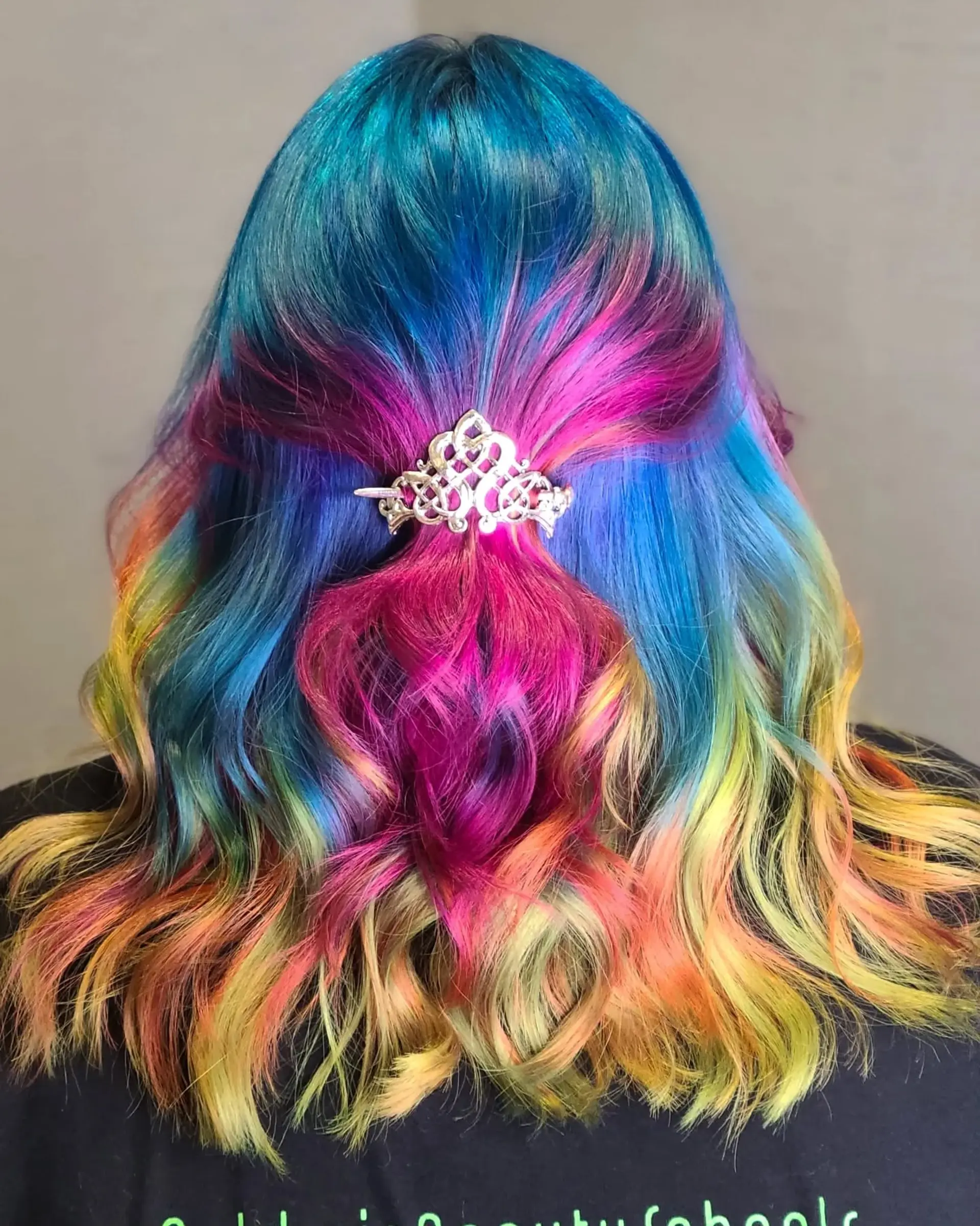 Long, wavy hair dyed in a striking rainbow palette of blues, pinks, purples, oranges, yellows, and greens, styled in a half-up twist secured with a decorative clip. 2