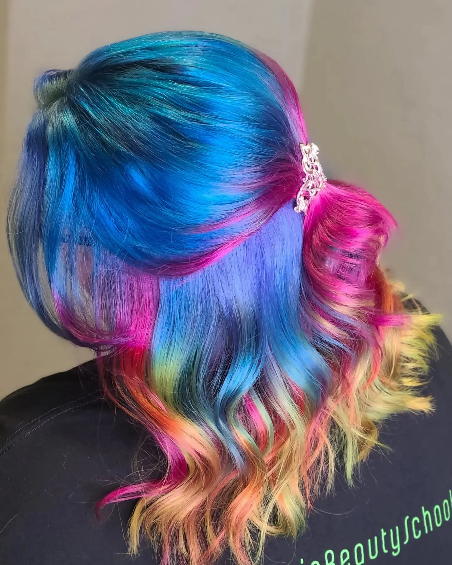 Long, wavy hair dyed in a striking rainbow palette of blues, pinks, purples, oranges, yellows, and greens, styled in a half-up twist secured with a decorative clip. 3