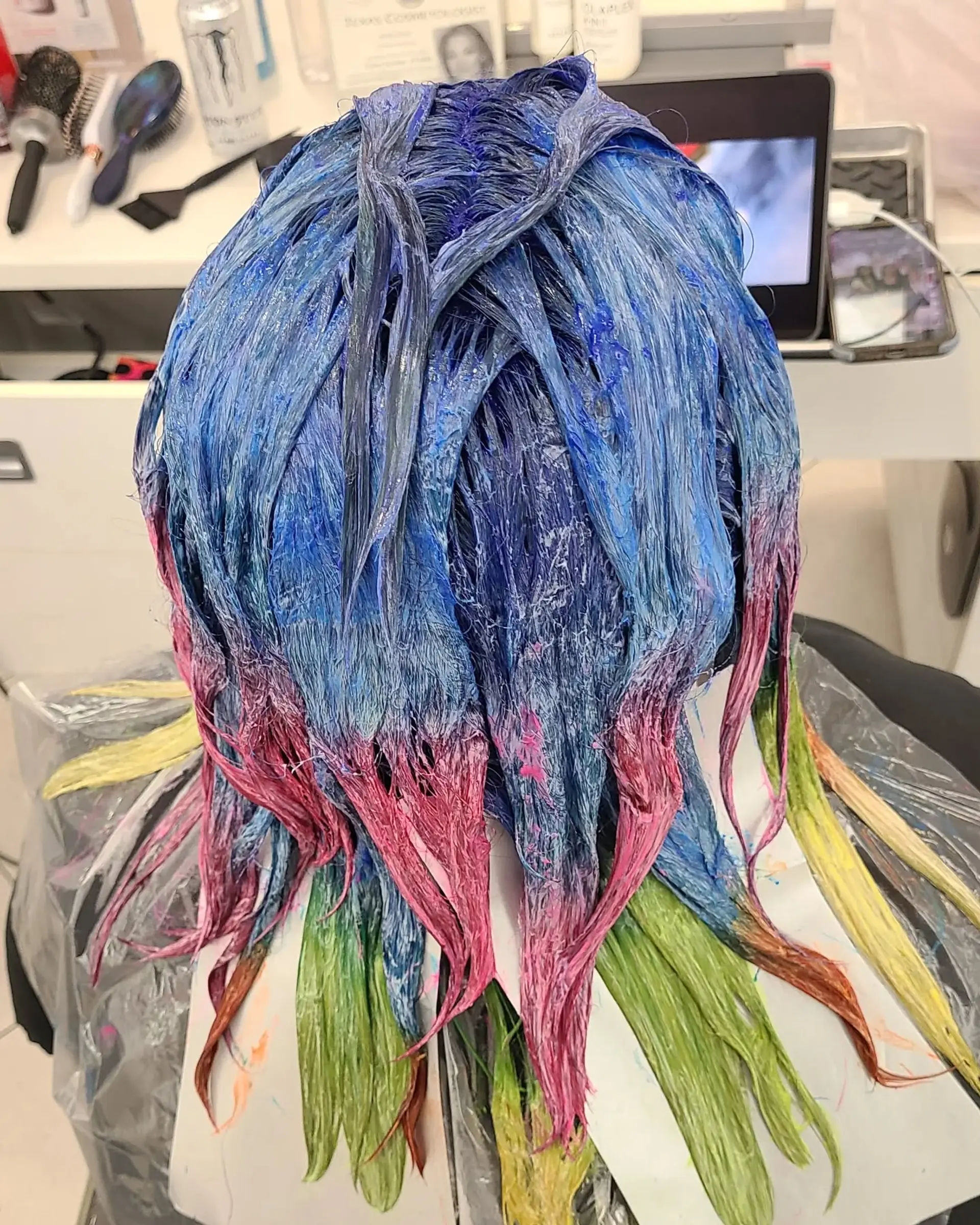 Long, wavy hair dyed in a striking rainbow palette of blues, pinks, purples, oranges, yellows, and greens, styled in a half-up twist secured with a decorative clip. 4