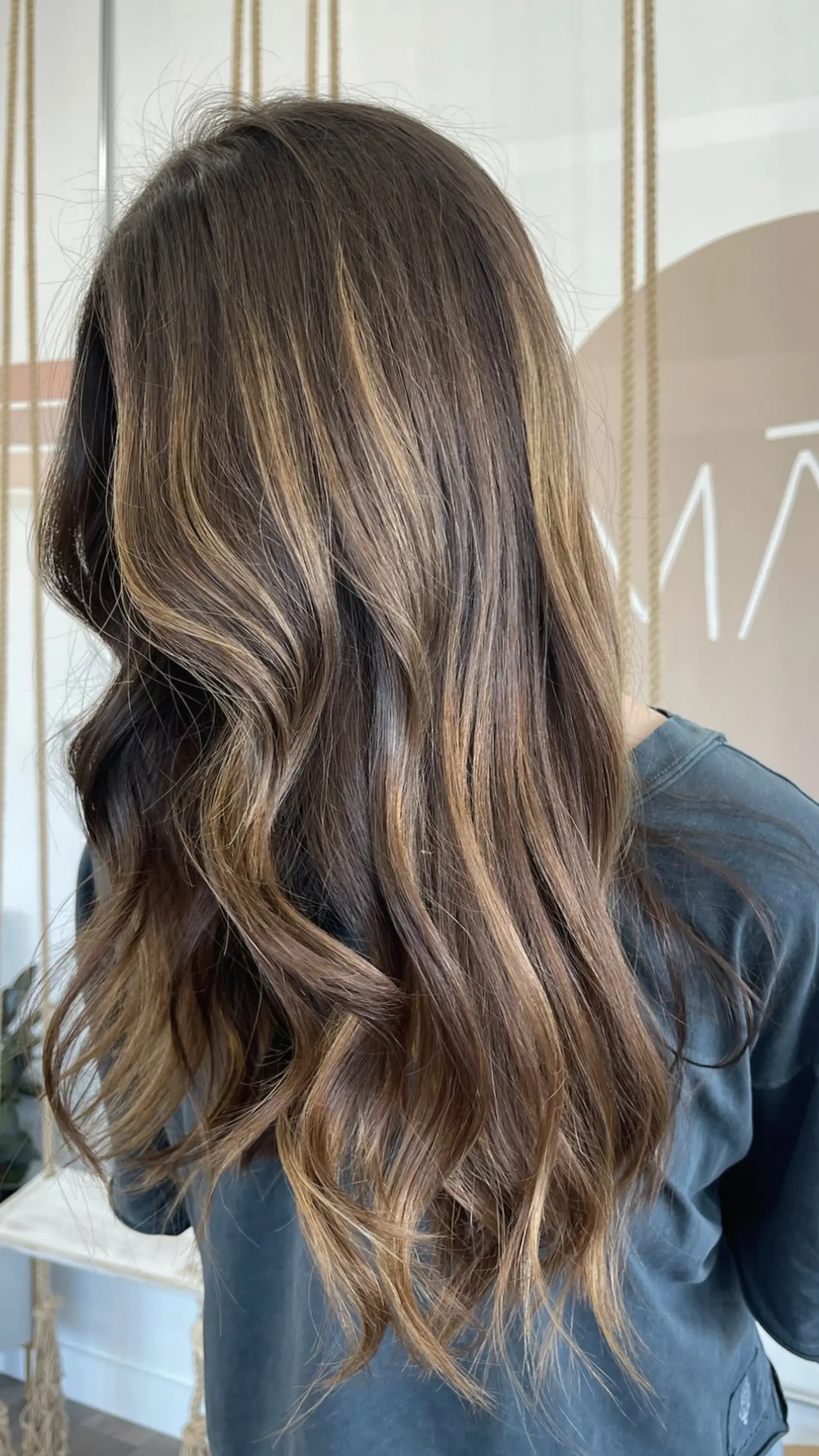 Long dimensional brunette hair with caramel highlights styled in soft, cascading waves. 1