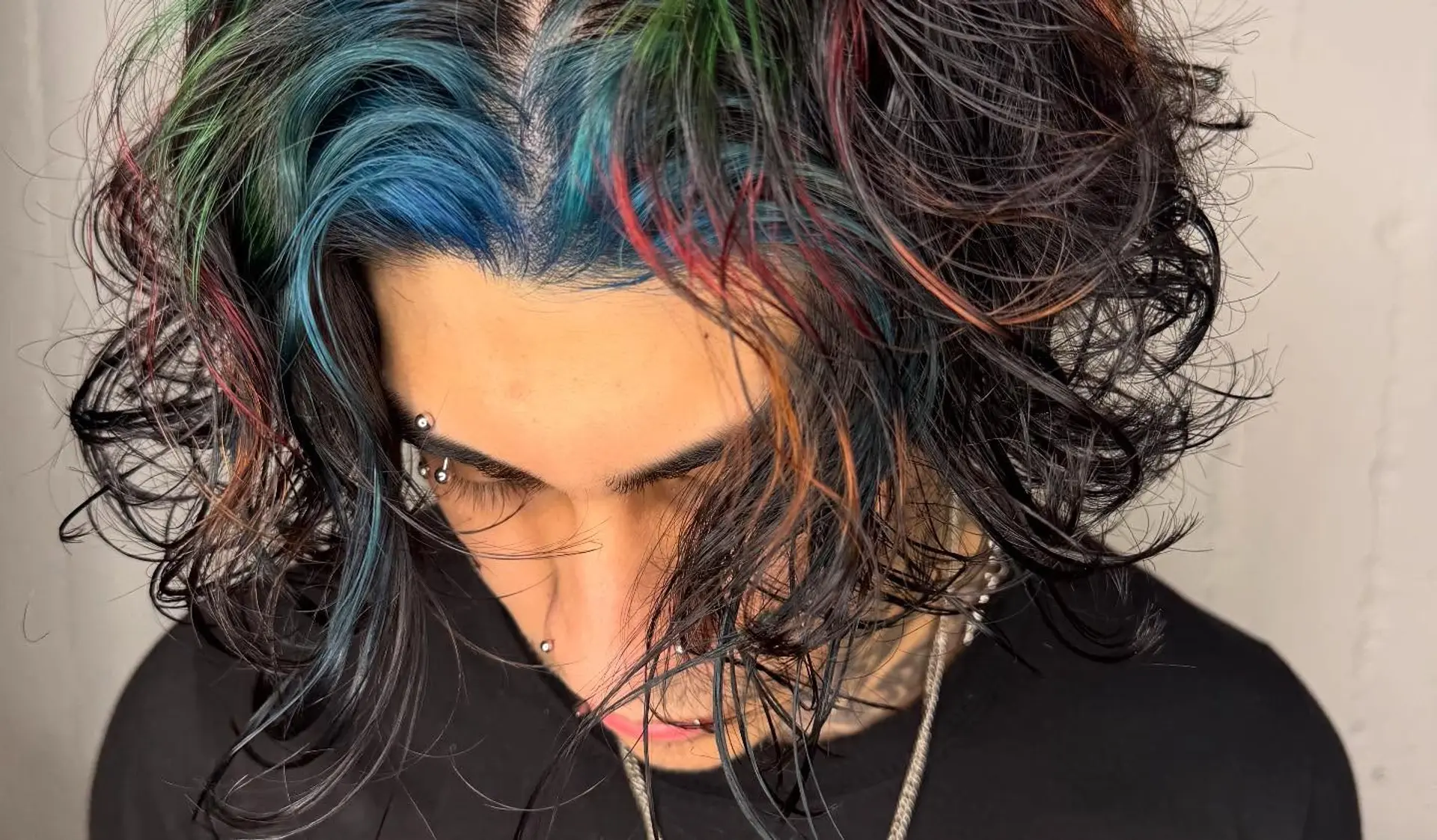 Tousled medium-length dark waves highlighted with vibrant streaks of blue, green, and red around the face and crown. 1