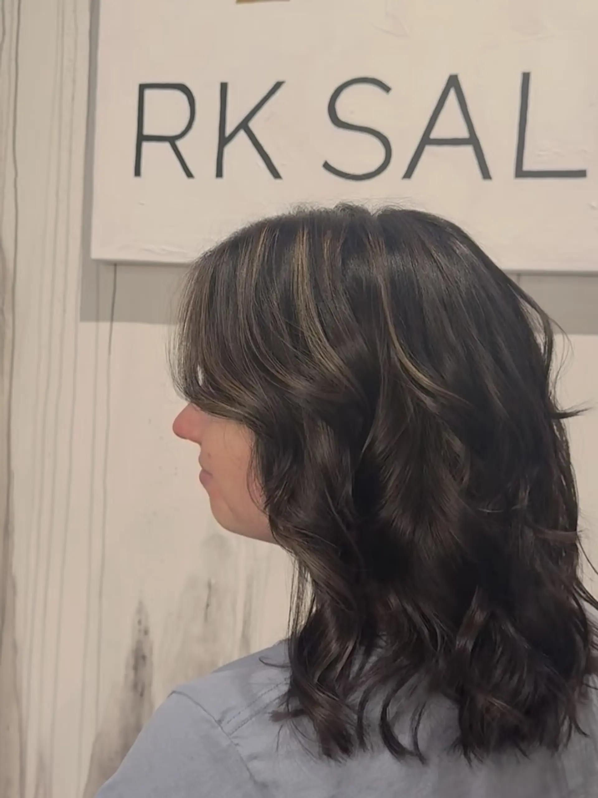 Medium-length dark brunette hair cut with soft face-framing layers, subtle dimensional highlights, and styled in loose waves. 1