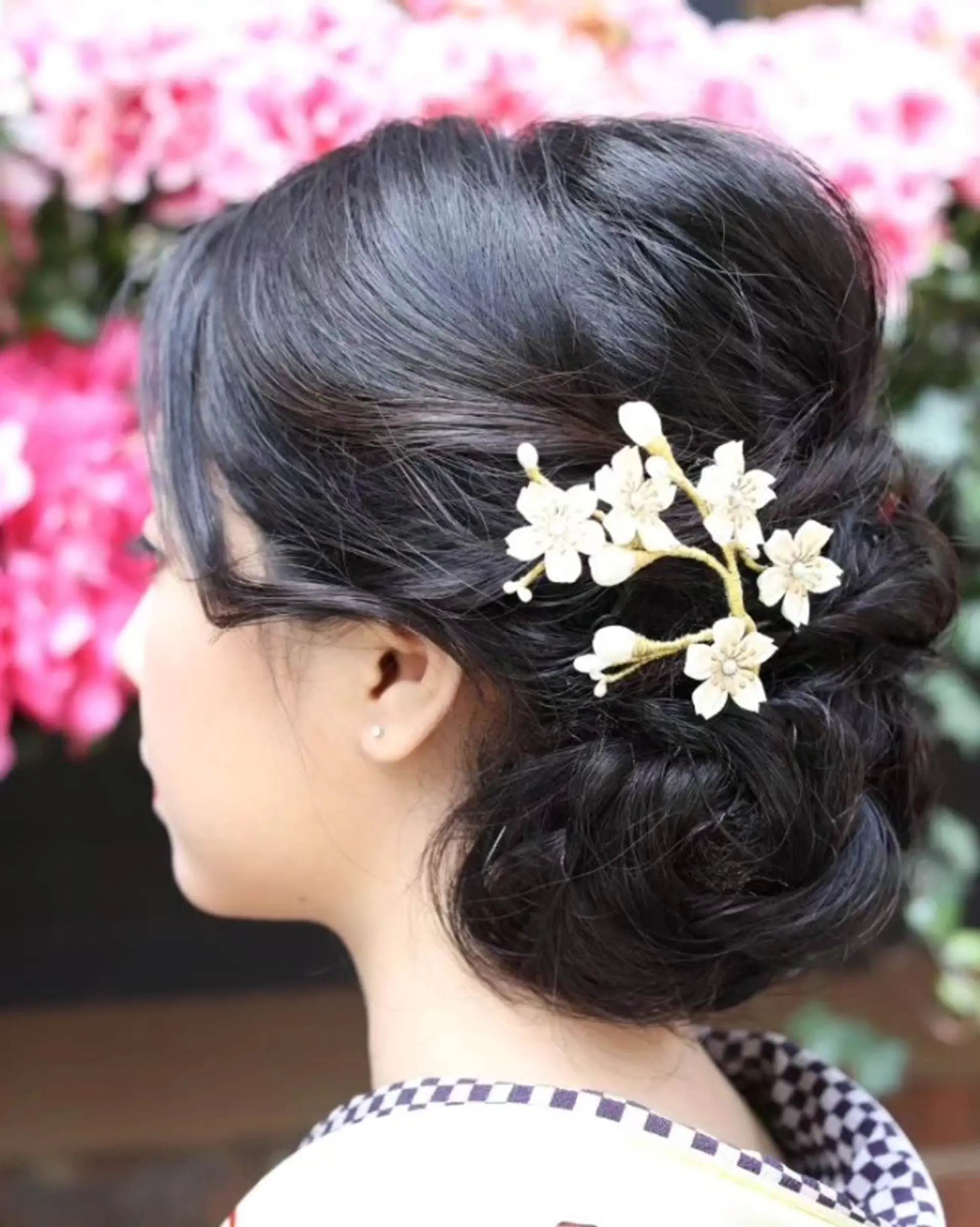 An elegant low bun updo arranged with soft twists and adorned with a delicate white floral hairpiece. 1