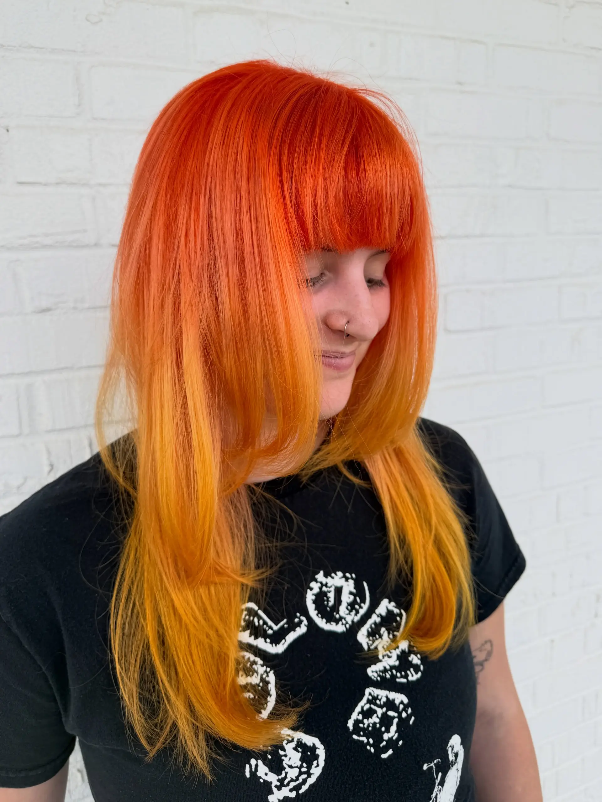 A vibrant vivid orange long hairstyle featuring full blunt bangs and soft face-framing layers. 1