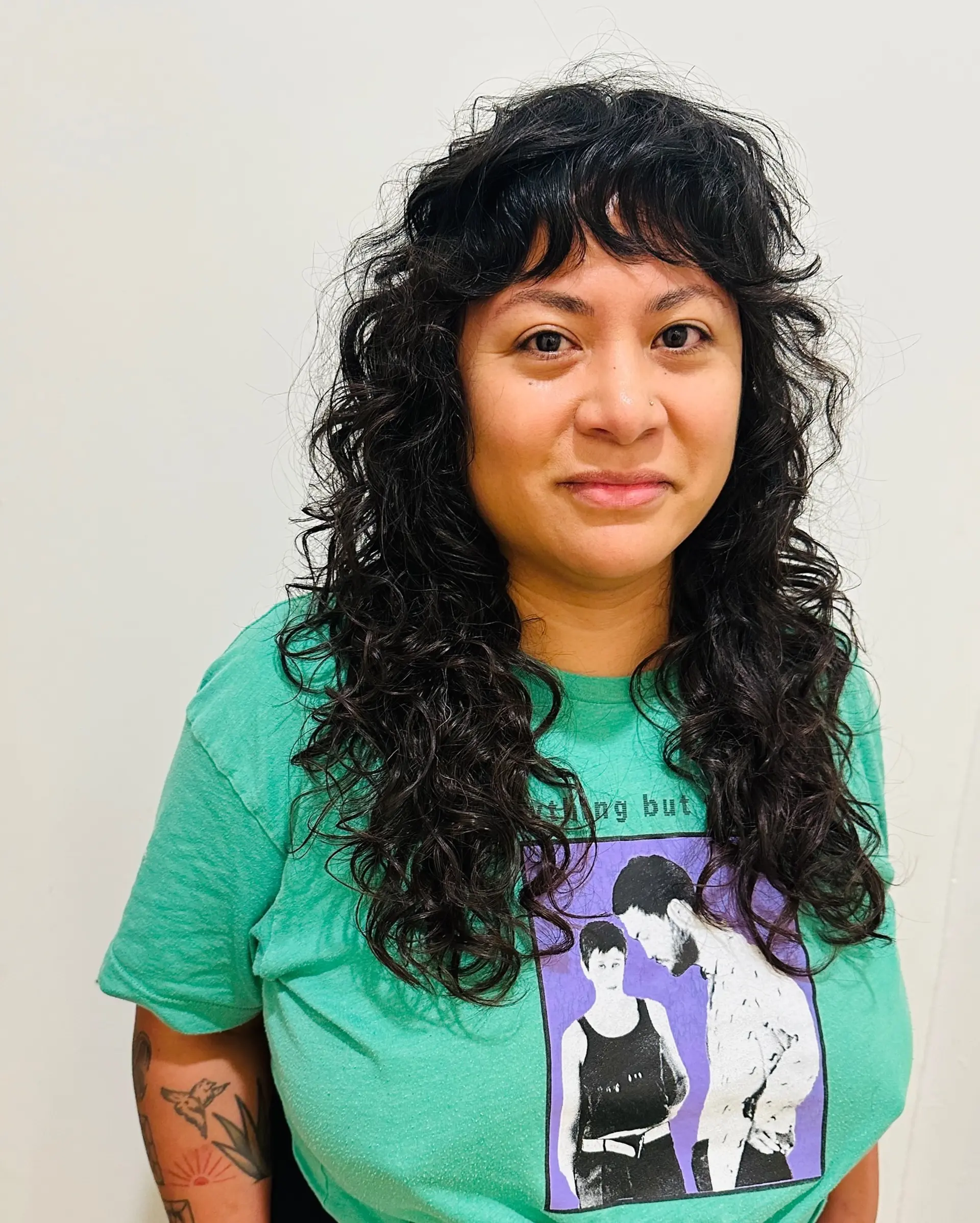 Long curly shag haircut featuring textured baby bangs and defined, layered curls. 1