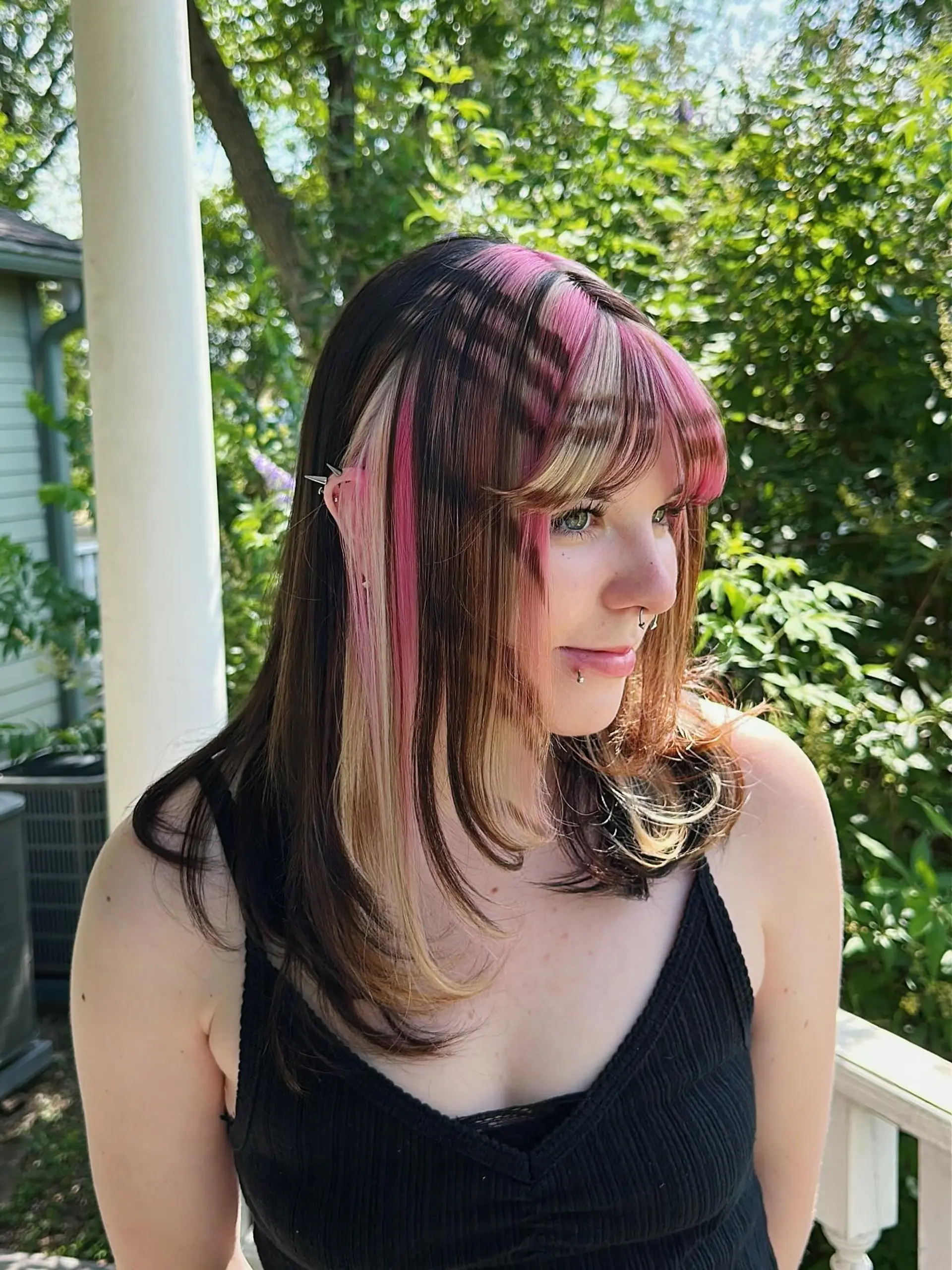 A medium-length cut with face-framing layers and full bangs, highlighted by striking chunky blonde and vivid pink panels against a dark brown base, creating a distinct color block effect. 1
