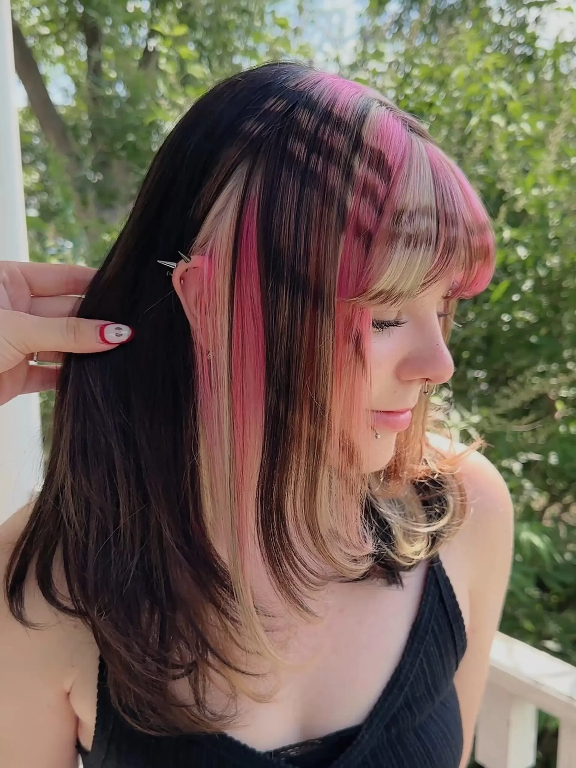 A medium-length cut with face-framing layers and full bangs, highlighted by striking chunky blonde and vivid pink panels against a dark brown base, creating a distinct color block effect. 3