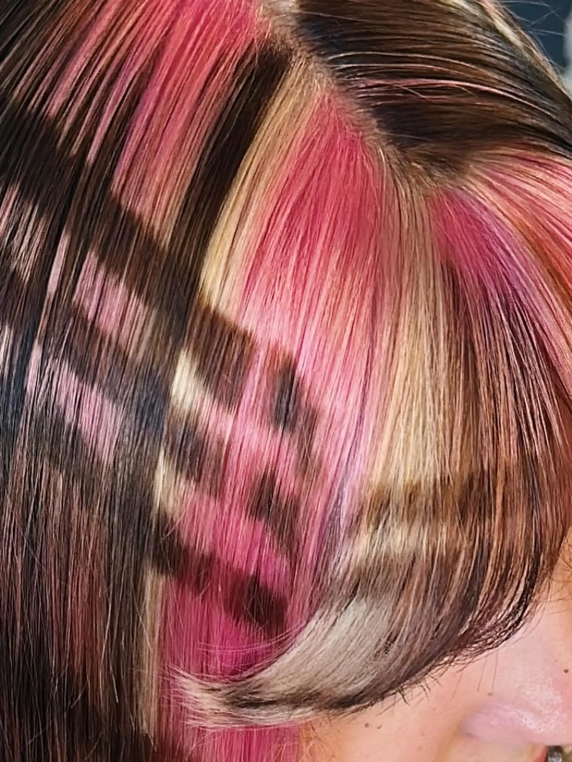 A medium-length cut with face-framing layers and full bangs, highlighted by striking chunky blonde and vivid pink panels against a dark brown base, creating a distinct color block effect. 4