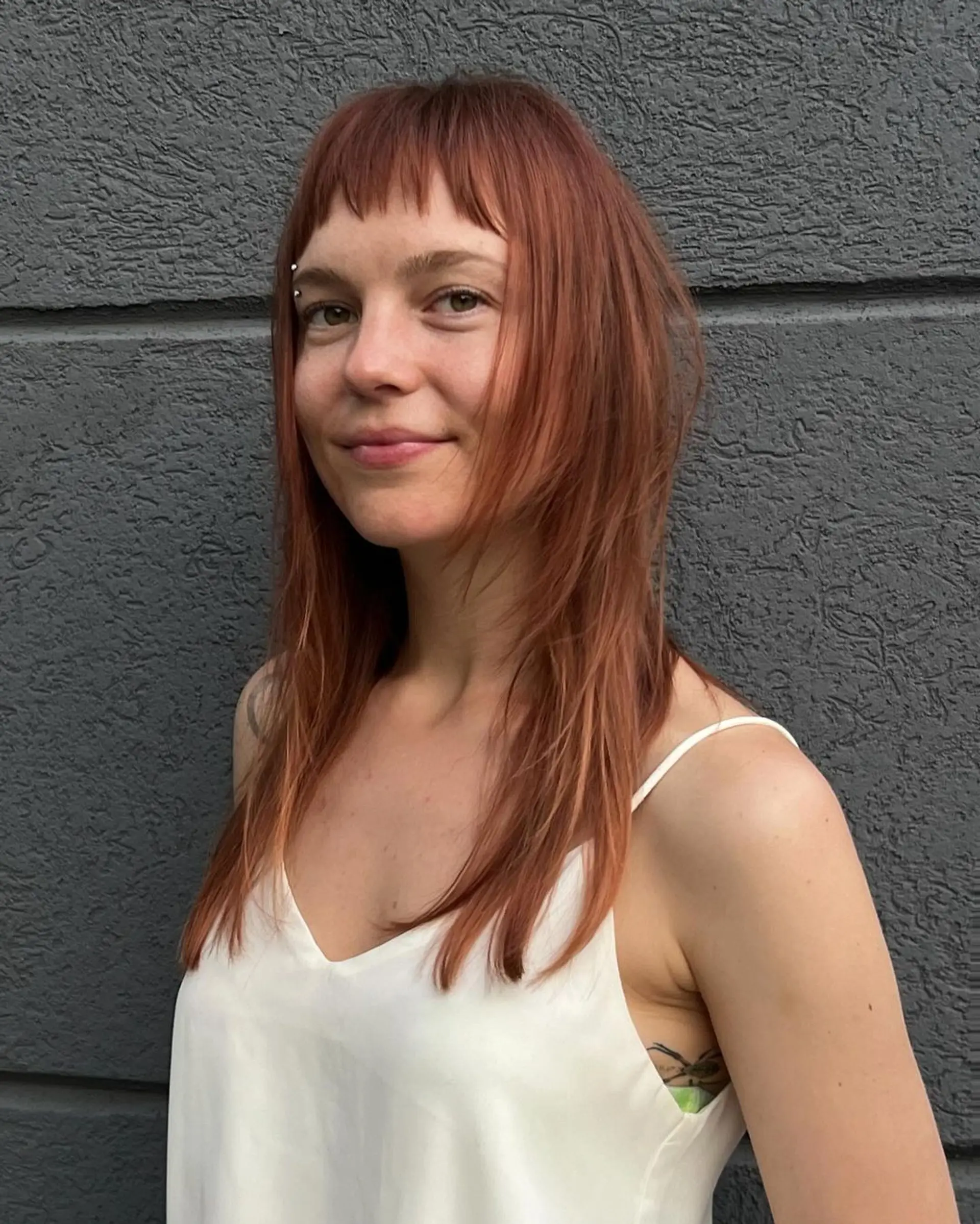 Long, straight auburn hair with blunt bangs resting above the eyebrows. Features face-framing locks and layered ends for added movement and lightness. 1