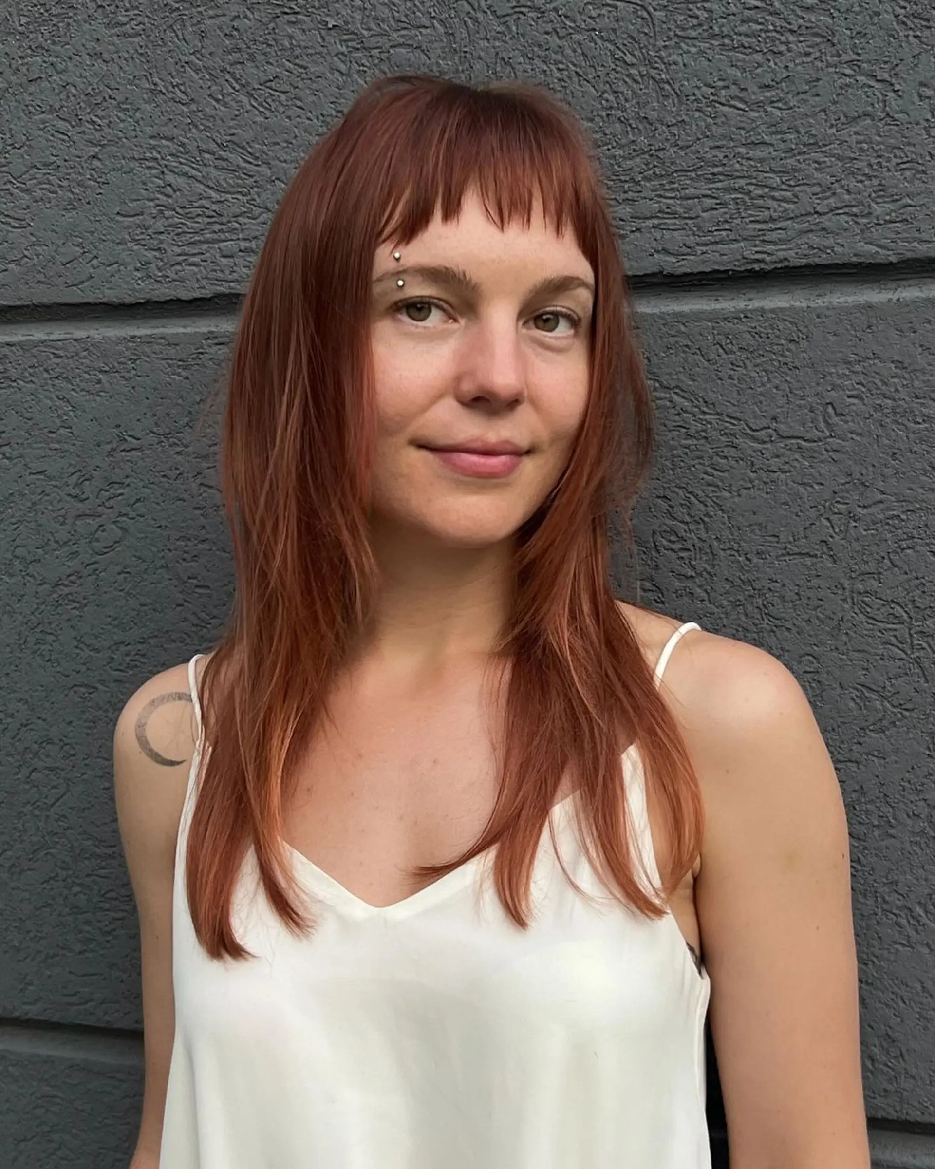 Long, straight auburn hair with blunt bangs resting above the eyebrows. Features face-framing locks and layered ends for added movement and lightness. 2