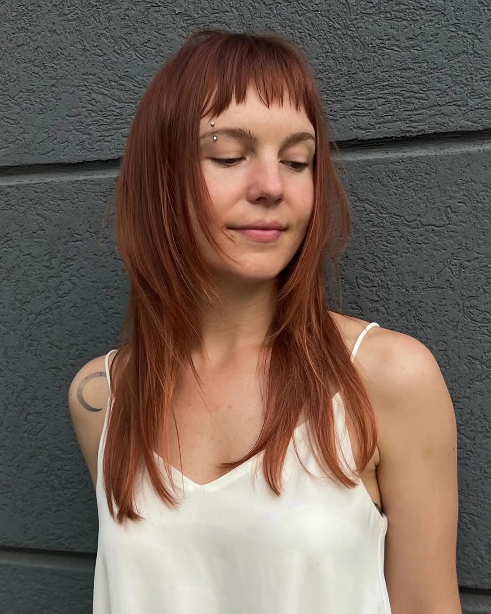 Long, straight auburn hair with blunt bangs resting above the eyebrows. Features face-framing locks and layered ends for added movement and lightness. 3