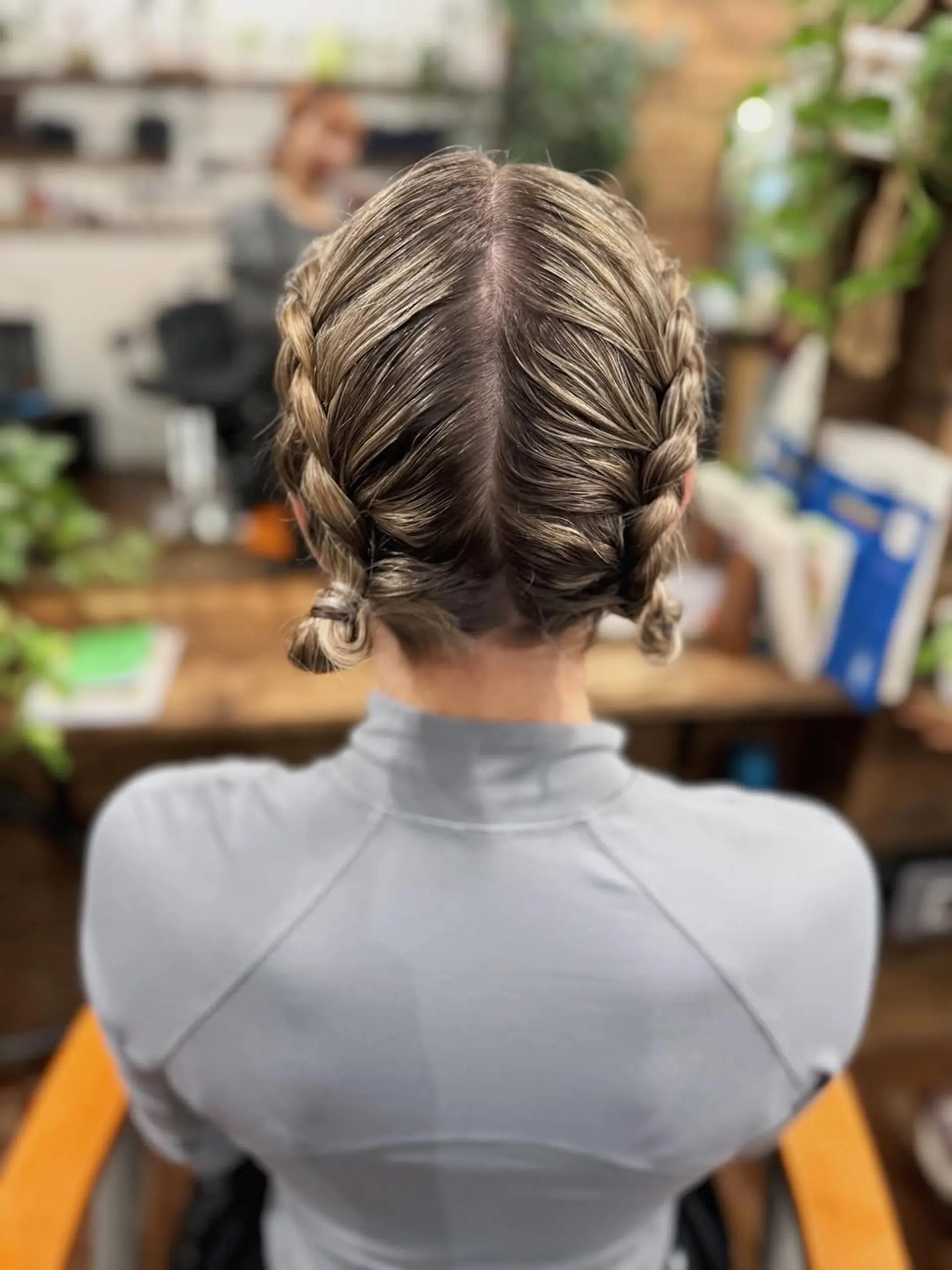 This style features two sleek Dutch braids, originating from a precise center part and extending down to the nape of the neck, where they are secured into neat, low coiled buns. 1