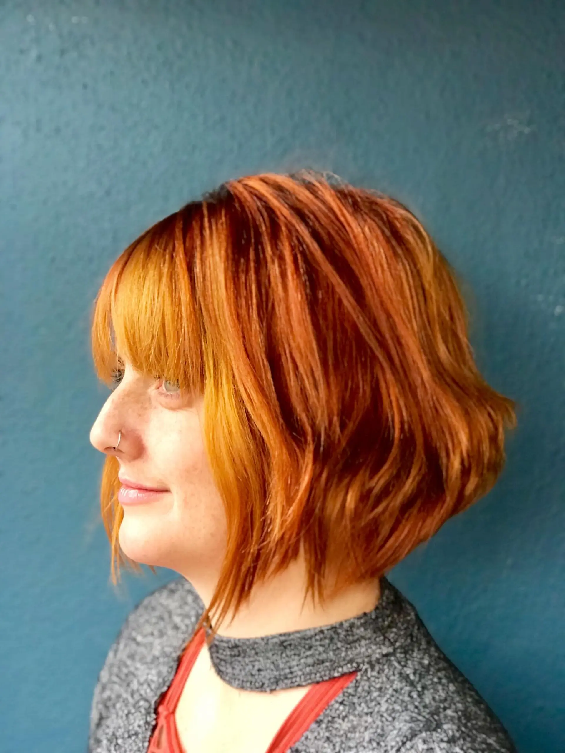 A textured angled bob cut with soft waves, full straight bangs, and vibrant copper-orange tones. 1