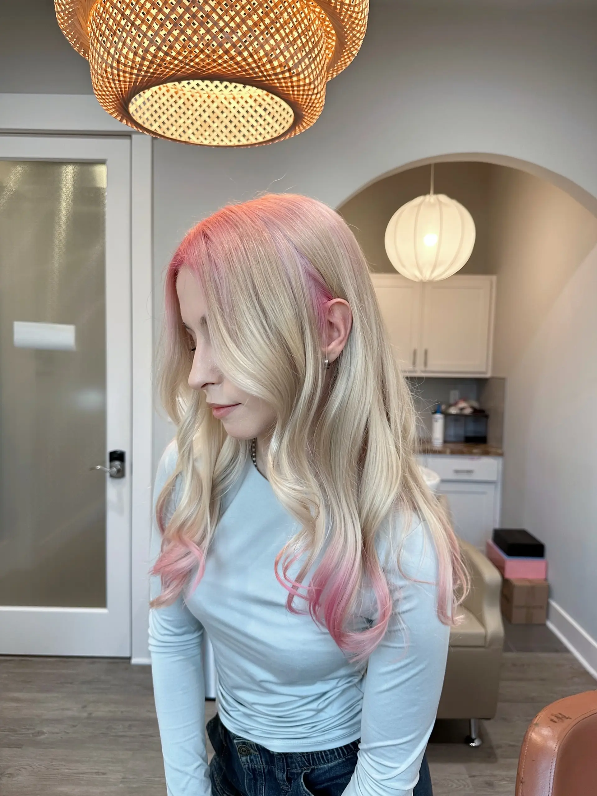 Long, flowing platinum blonde hair styled in soft waves, complemented by a seamless pastel pink root melt that gradually blends into the blonde, with hints of pink also visible towards the ends. 3