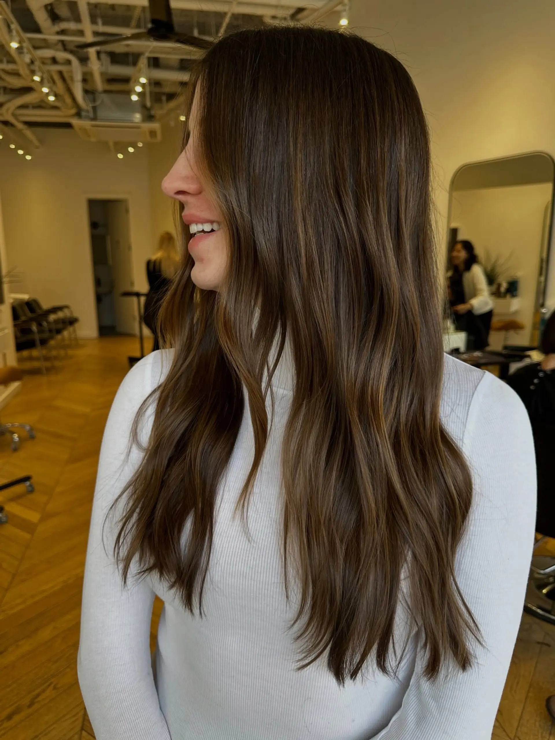 Long dark brown hair cut with soft layers, styled in gentle waves with subtle warm bronde highlights. 1