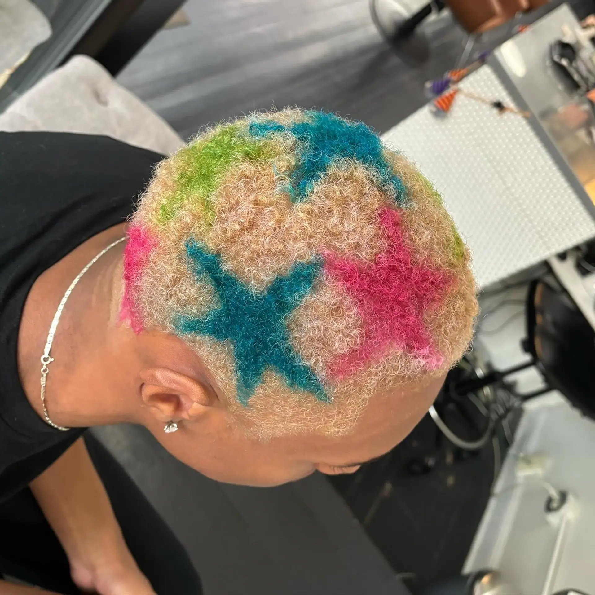 A bleached blonde buzz cut styled with vibrant multicolor star designs painted across the top and sides. 1