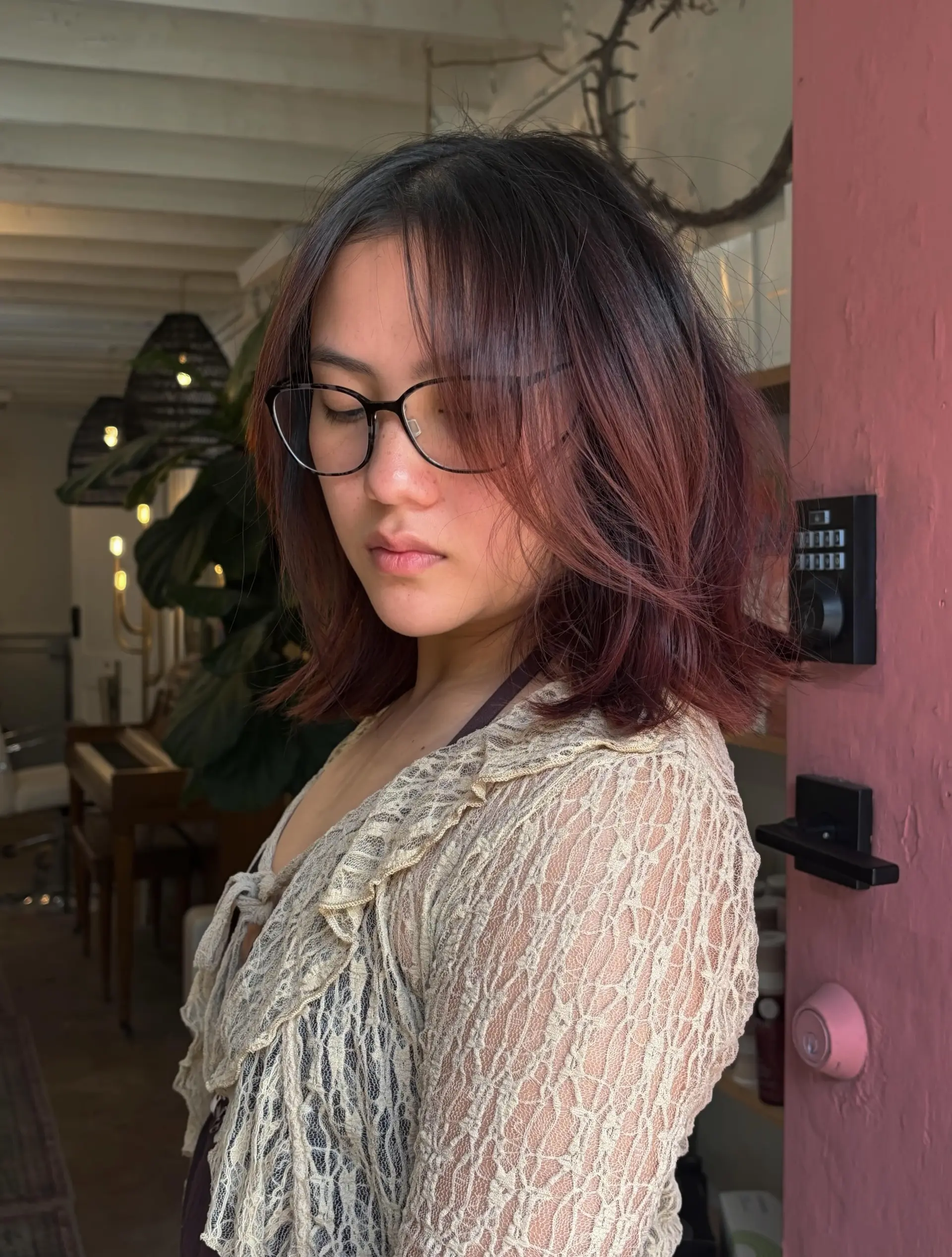 A textured, collarbone-grazing bob haircut with soft face-framing layers and wispy bangs, finished with subtle rose-tinted brunette dimension. 1