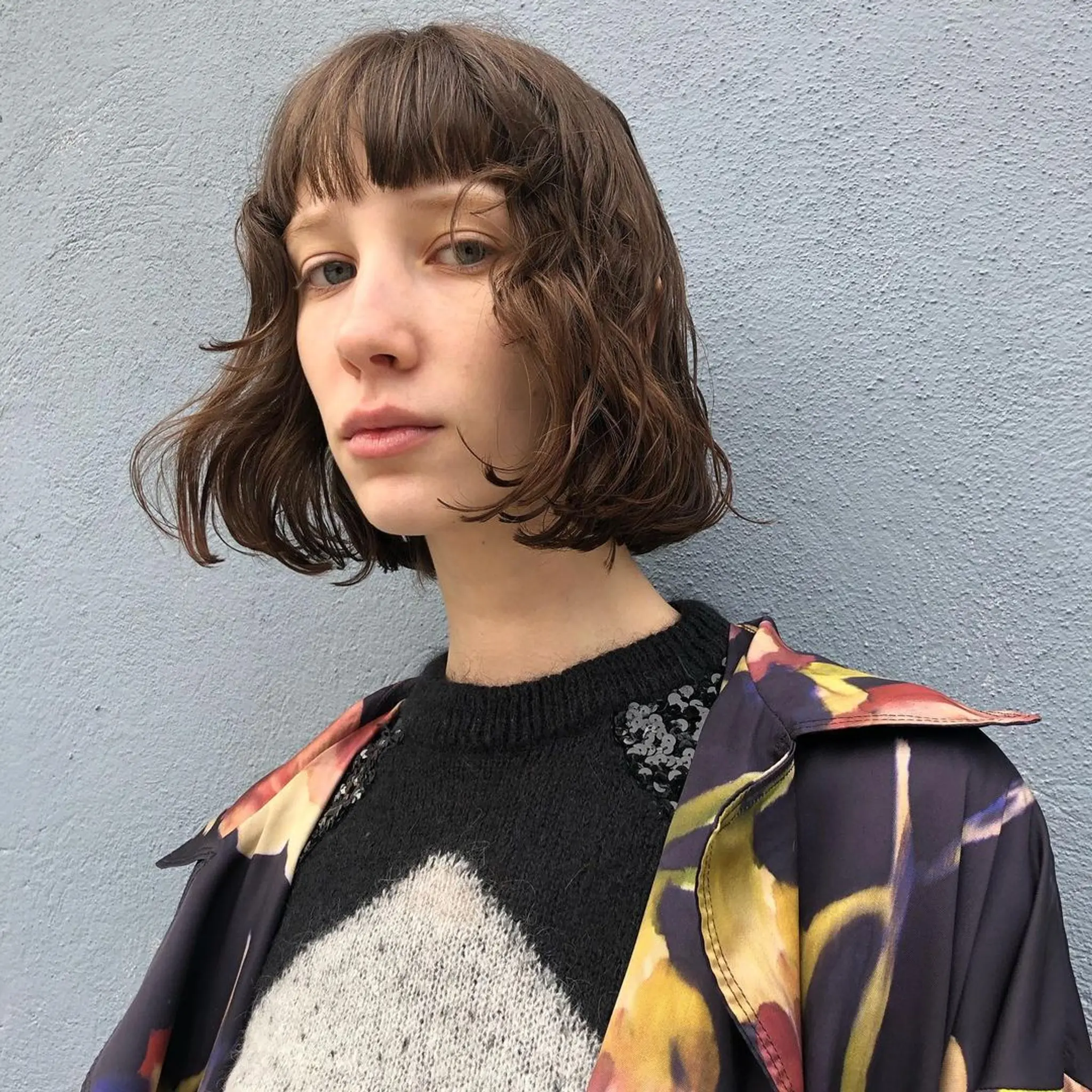 A short, wavy bob with messy waves and a blunt fringe, featuring textured ends and casual face-framing layers.