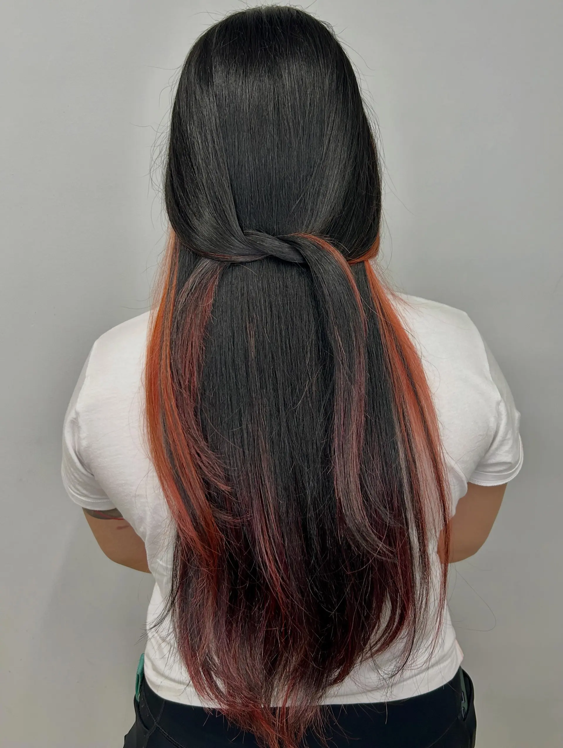 Long, sleek black hair styled with a half-up crossover twist showcasing copper-red peek-a-boo underlights. 1