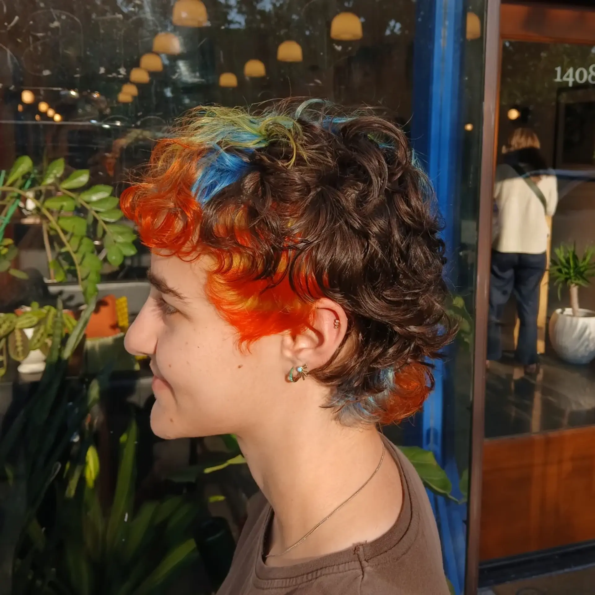A textured curly mullet featuring vivid blocks of fiery orange, bright blue, and yellow contrasting against deep brown curls. 1