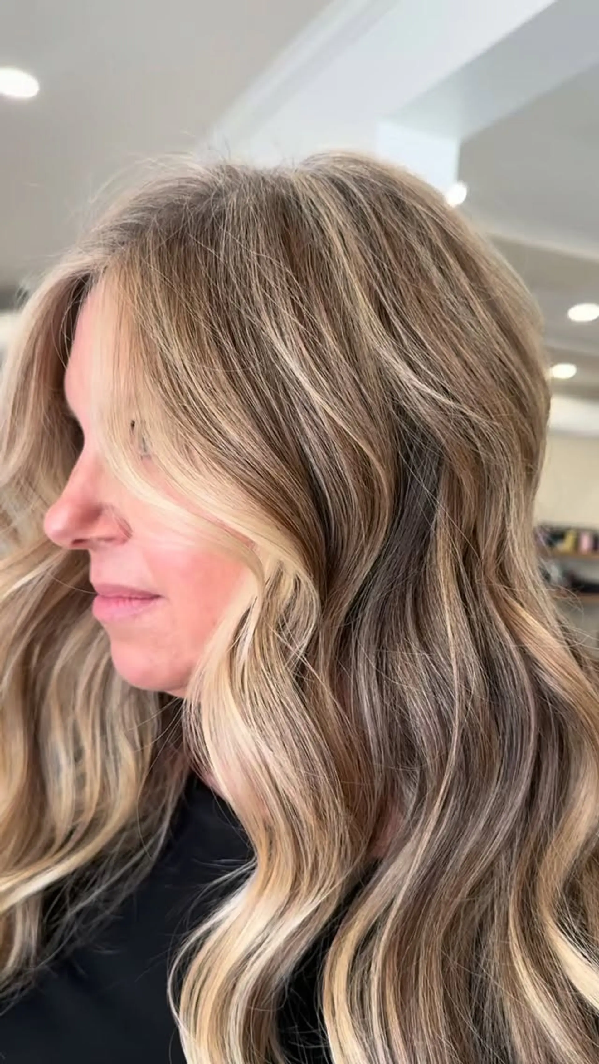 Long dimensional blonde hair styled into smooth, loose waves with face-framing brighter pieces. 1