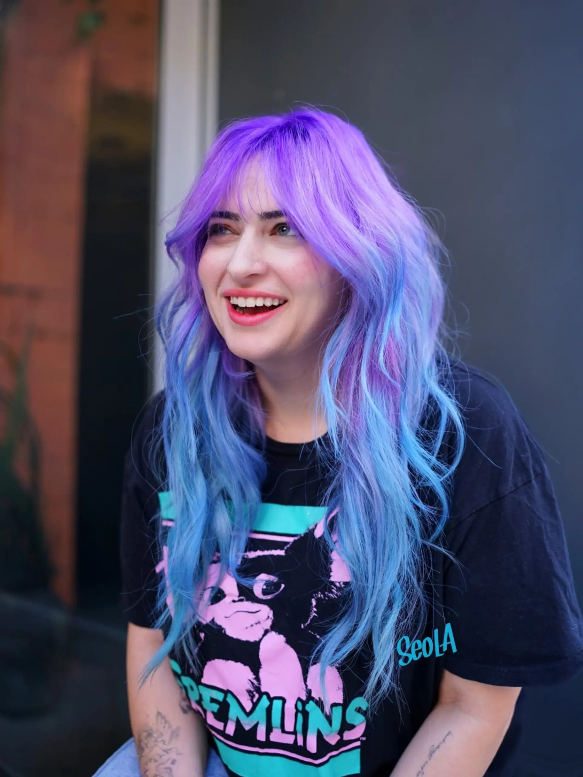 Long, tousled wavy hairstyle featuring wispy curtain bangs and a vibrant color melt transitioning from bright lavender-purple to electric blue. 1