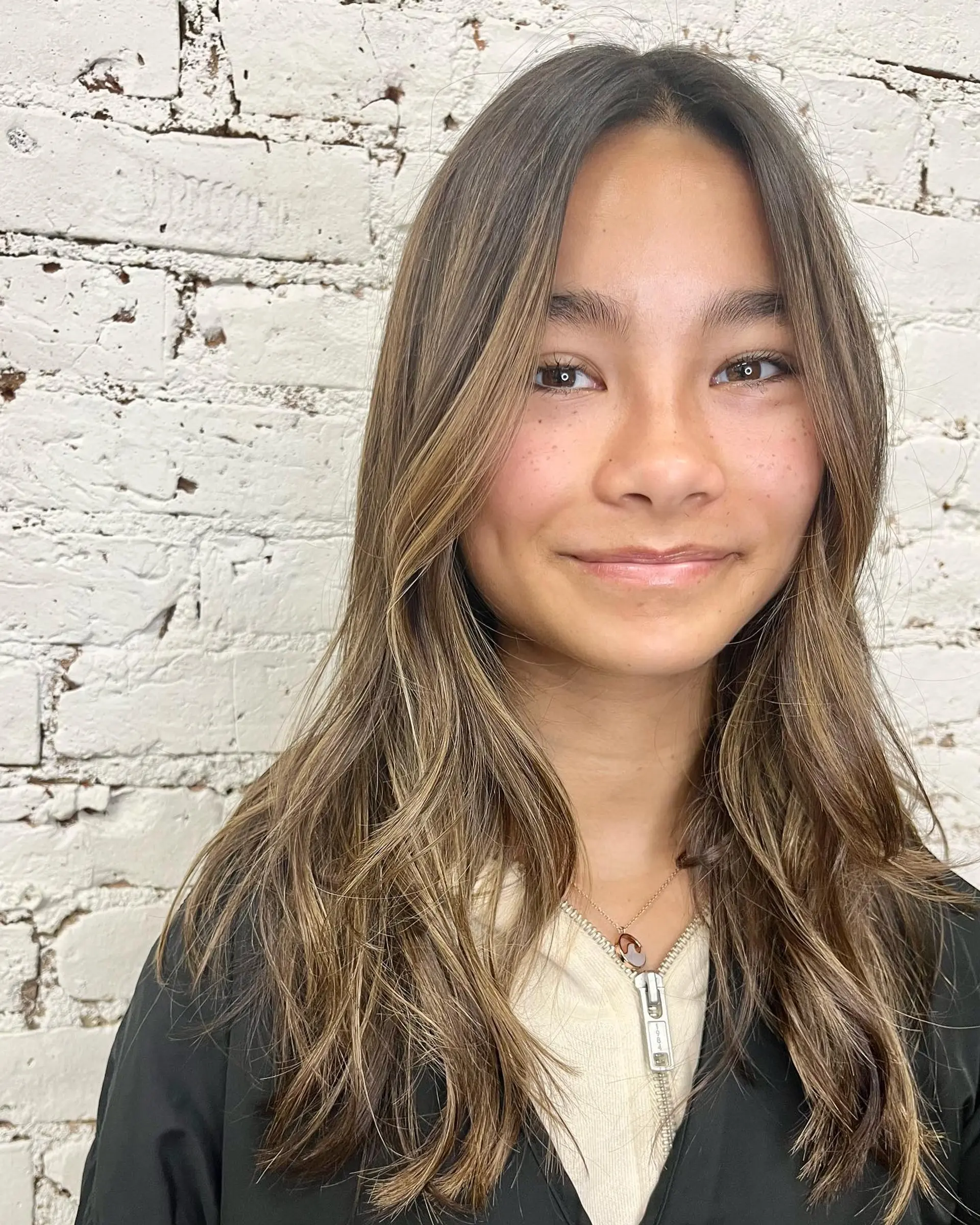 Long brown hair styled with soft, natural waves, face-framing layers, and delicate balayage highlights. 1