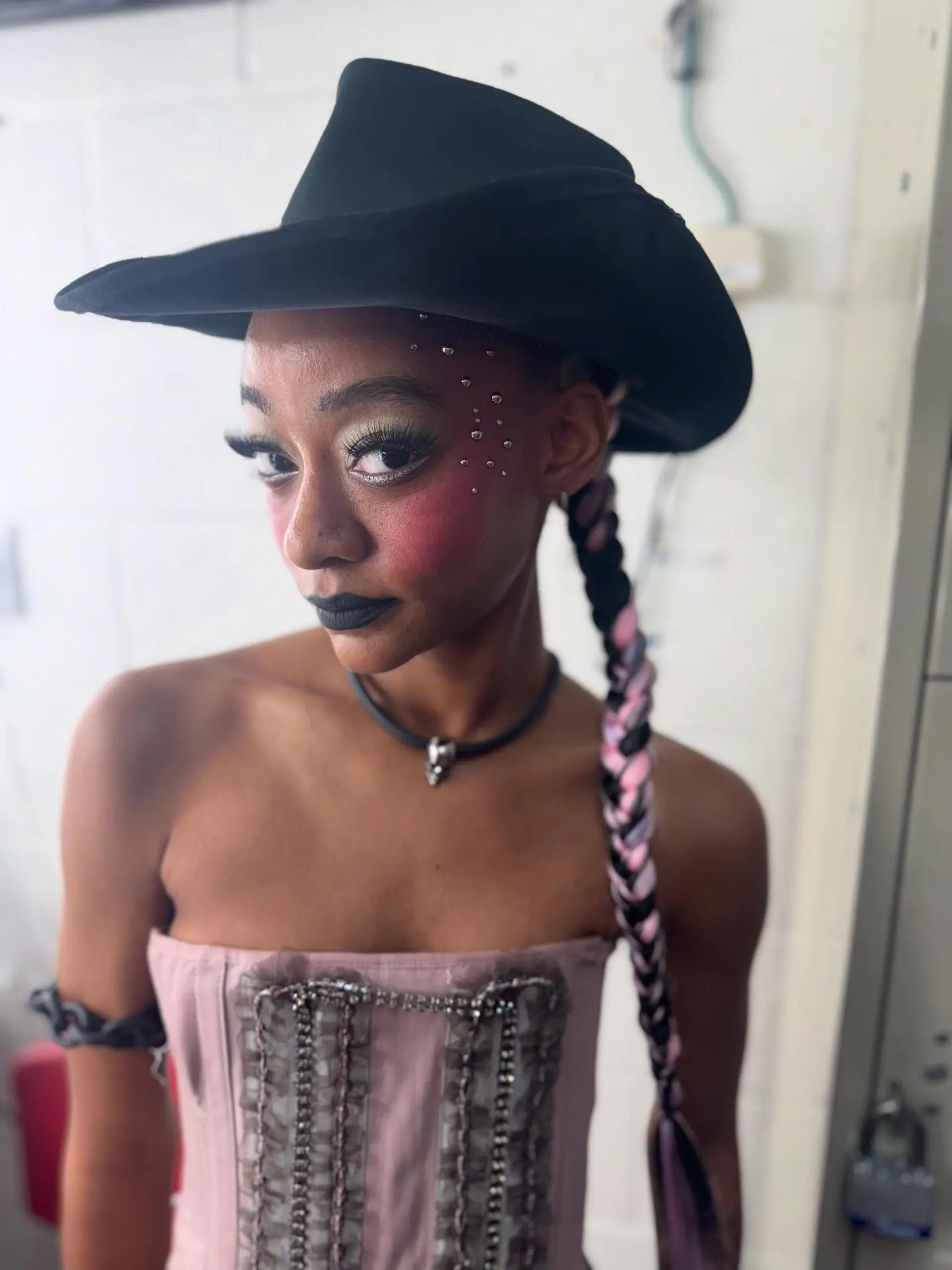 A sleek, ultra-long side braid interwoven with pastel pink and lavender accent pieces, styled beneath a black western hat. 1