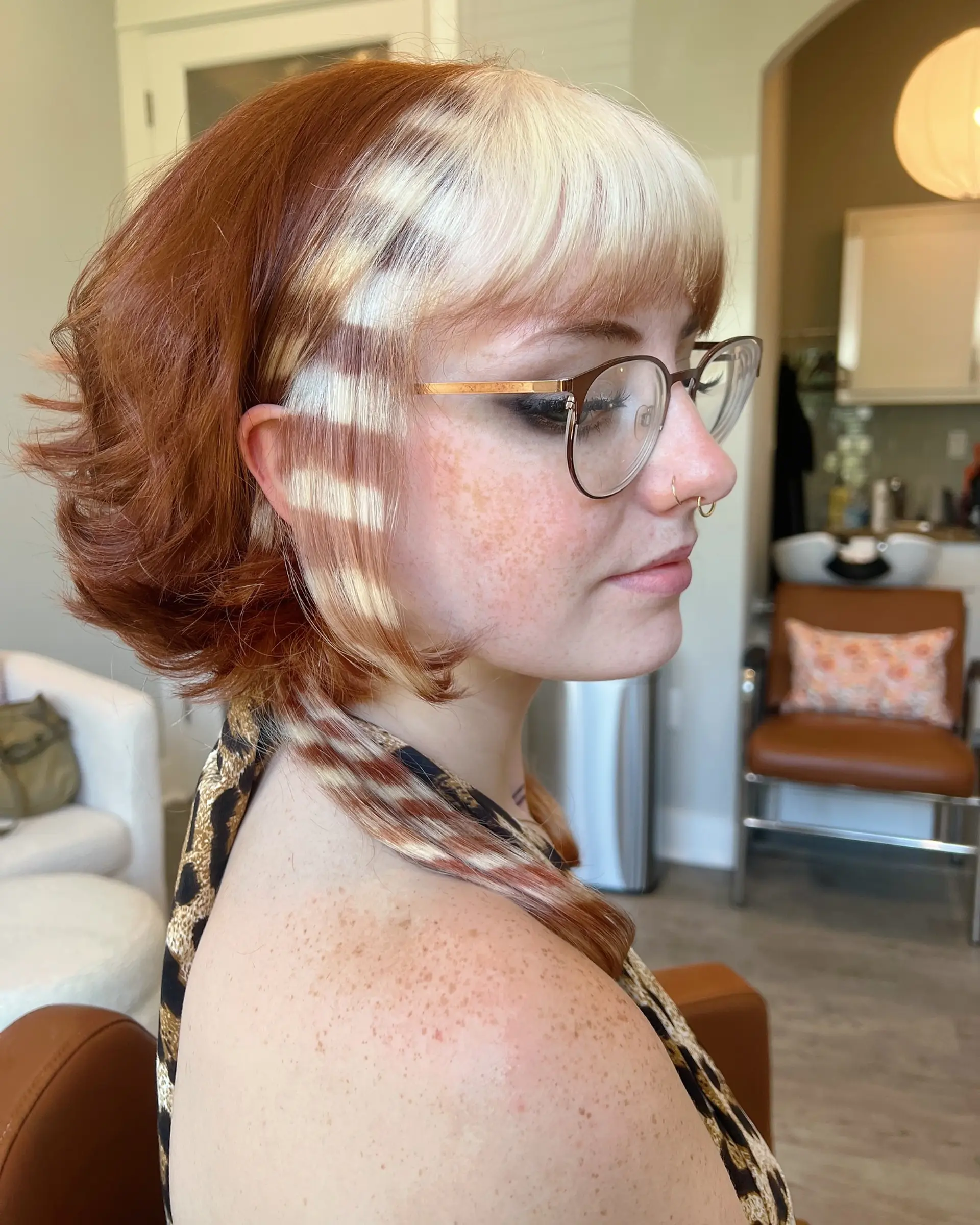 A choppy, layered short shag haircut with face-framing bangs, styled with defined waves. The hair is colored with a creative leopard print design, combining auburn and light blonde tones, including unique patterned strands. 3