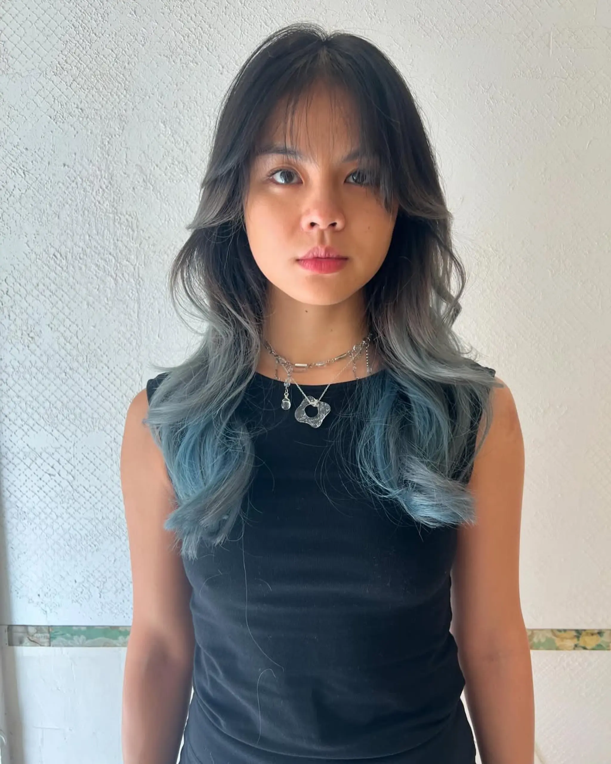 Long, wavy two-tone hair with black roots transitioning into blue, styled with soft waves and face-framing layers.