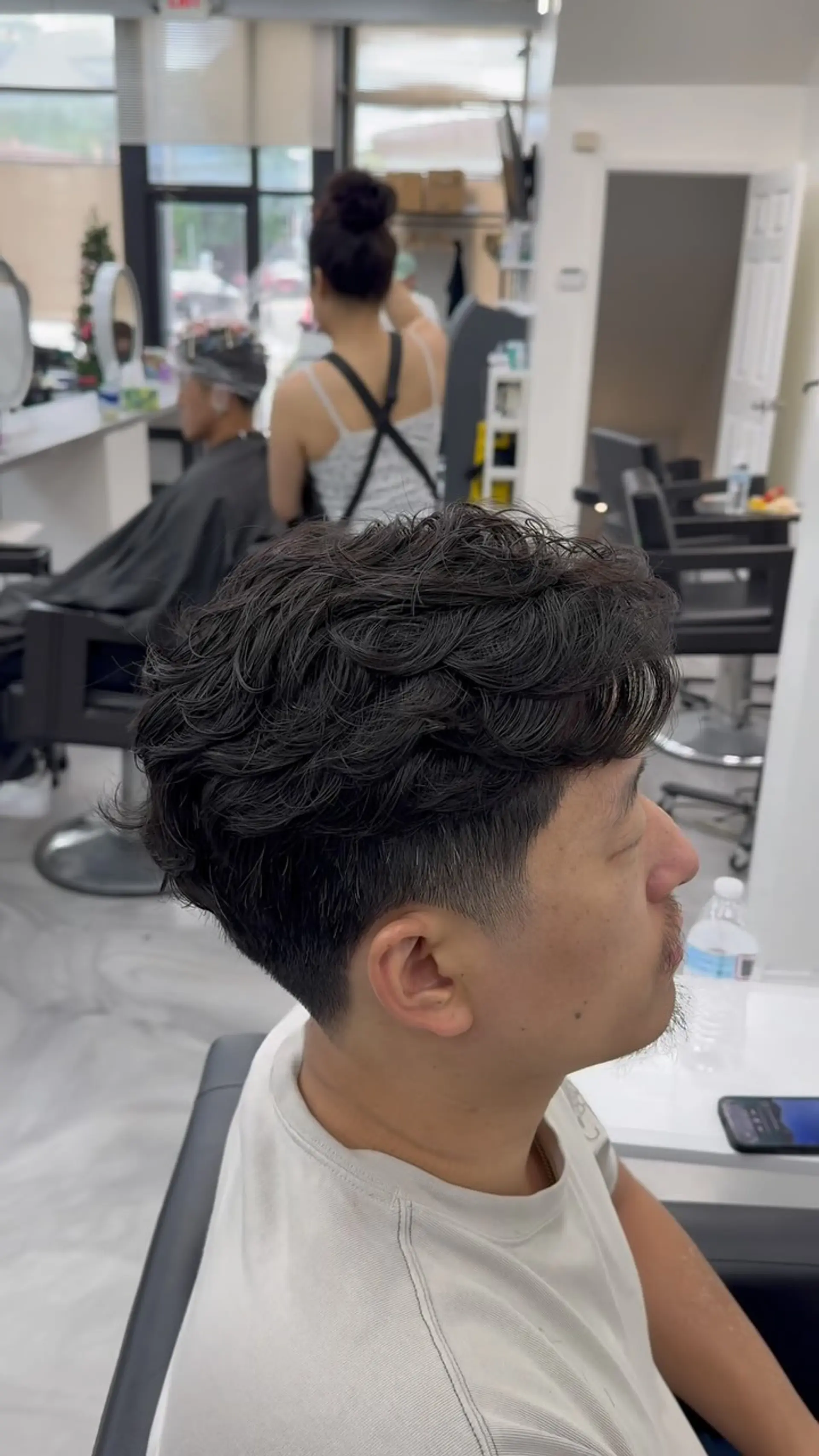 A men's short haircut showcasing a clean low fade on the sides paired with soft, textured perm waves on top. 1