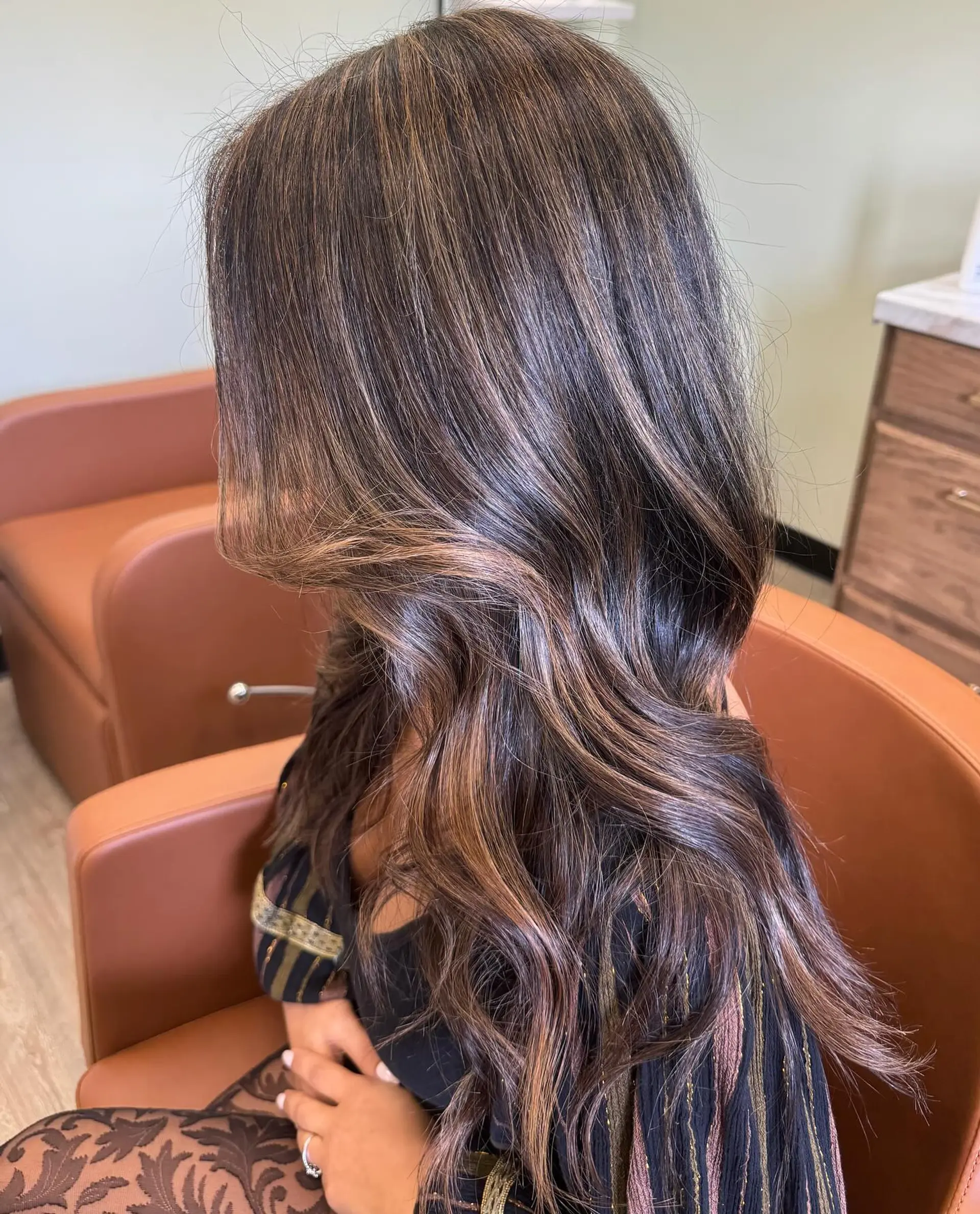 Long dark brown hair enhanced with seamless caramel balayage highlights and styled into soft, luminous waves. 1