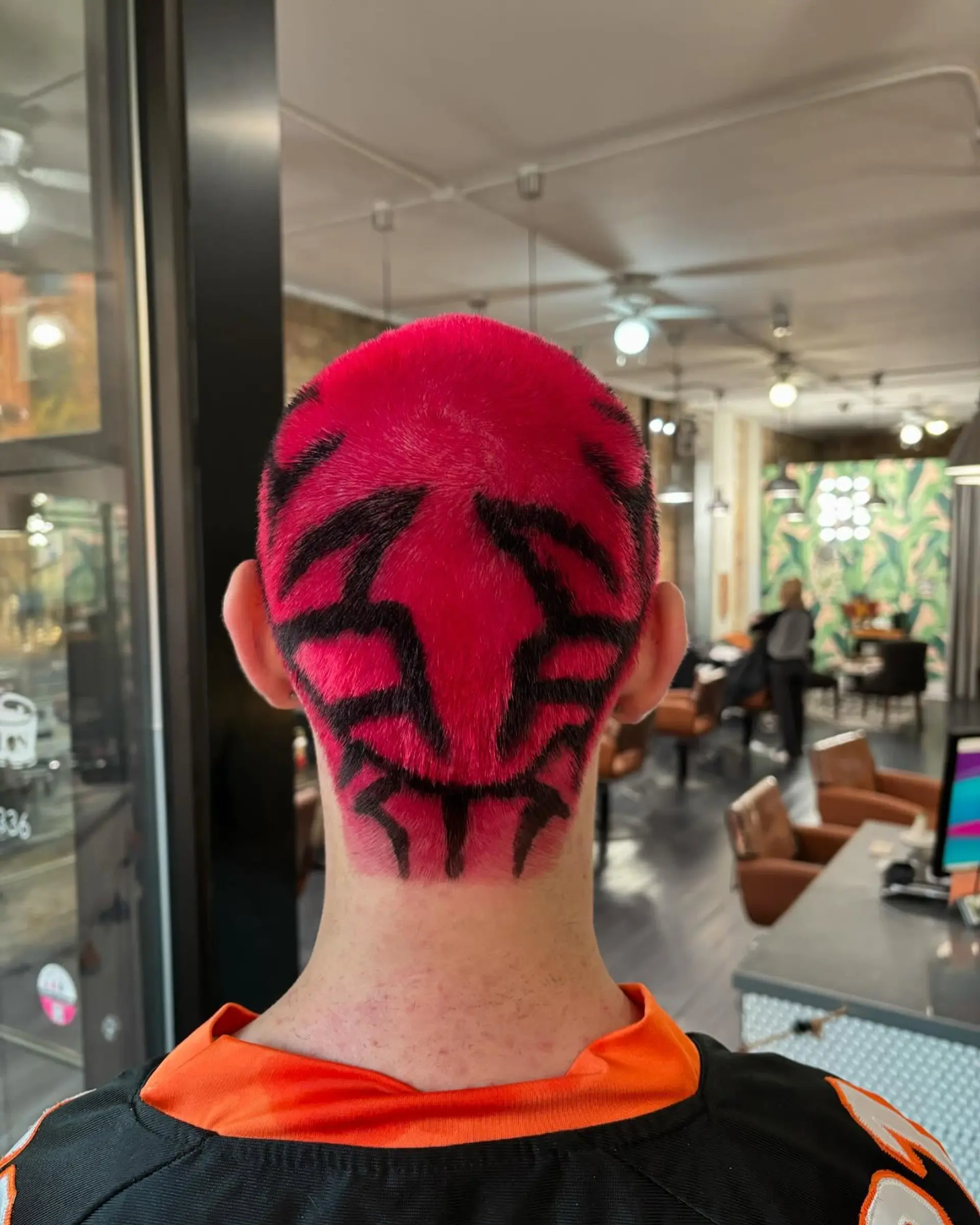 A vibrant hot pink buzz cut featuring a hand-painted black tribal-inspired graphic design across the back of the head. 1