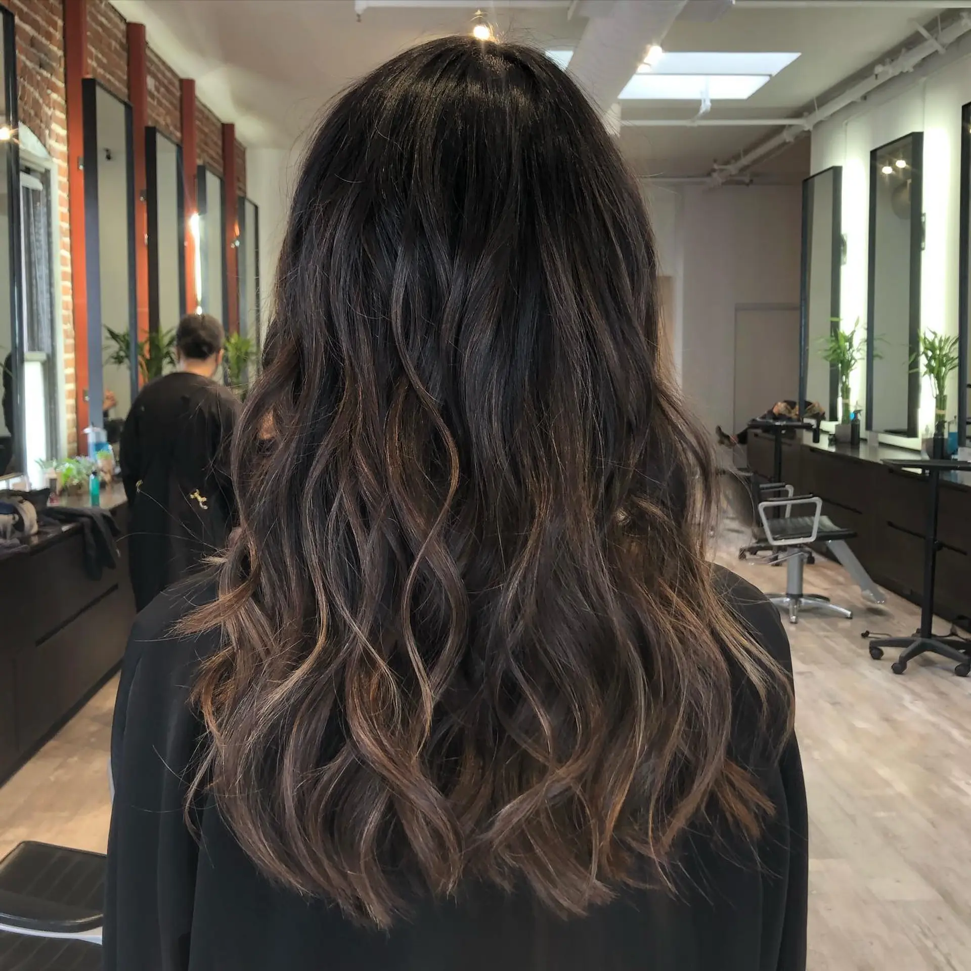 Long dark brown hair enhanced with subtle caramel balayage highlights and styled into soft, relaxed waves. 1