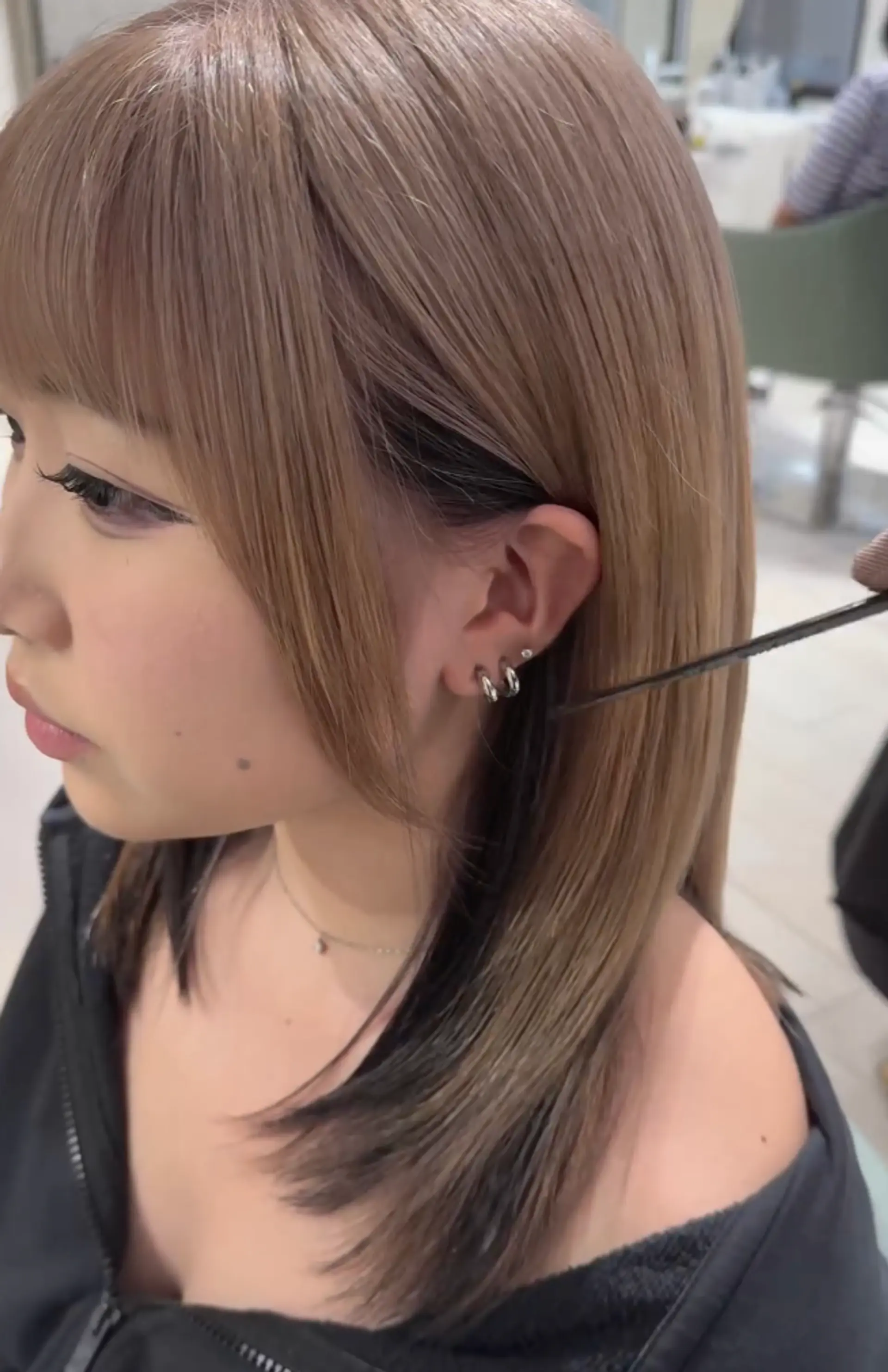 The hairstyle features sleek, straight ash brown hair that falls to medium length, with blunt bangs and a black underlayer, creating a two-toned, multi-dimensional look. 1