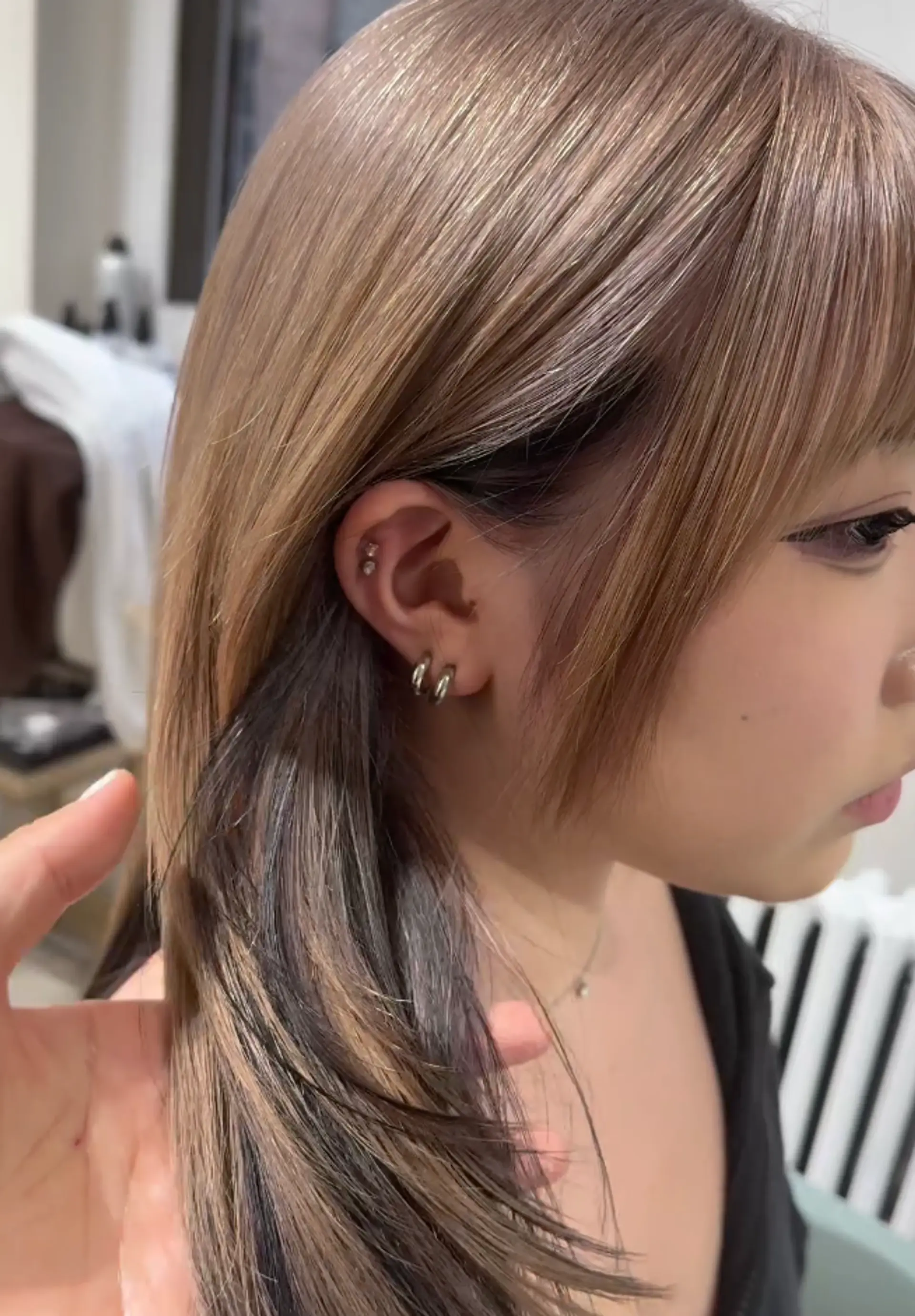 The hairstyle features sleek, straight ash brown hair that falls to medium length, with blunt bangs and a black underlayer, creating a two-toned, multi-dimensional look. 2