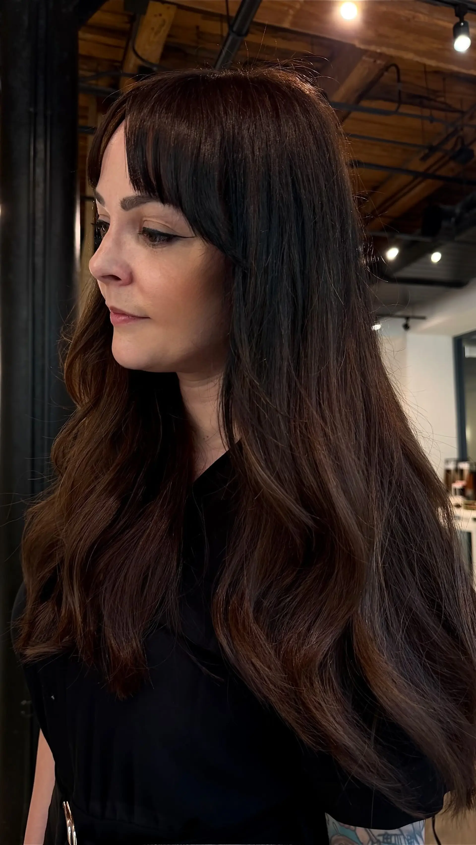 Long, rich dark brown hair styled with soft loose waves and straight-across fringe bangs. 1