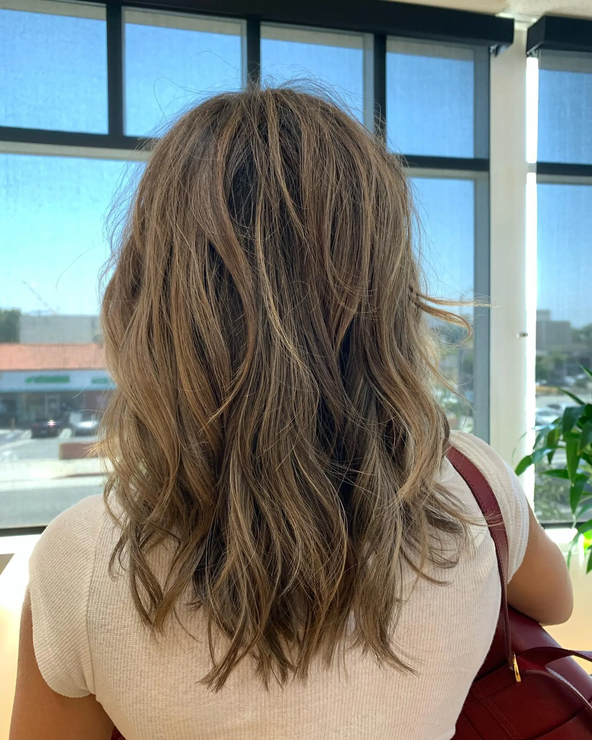 Long layered ash brown hair enhanced with subtle blonde highlights and styled in soft, textured waves. 1