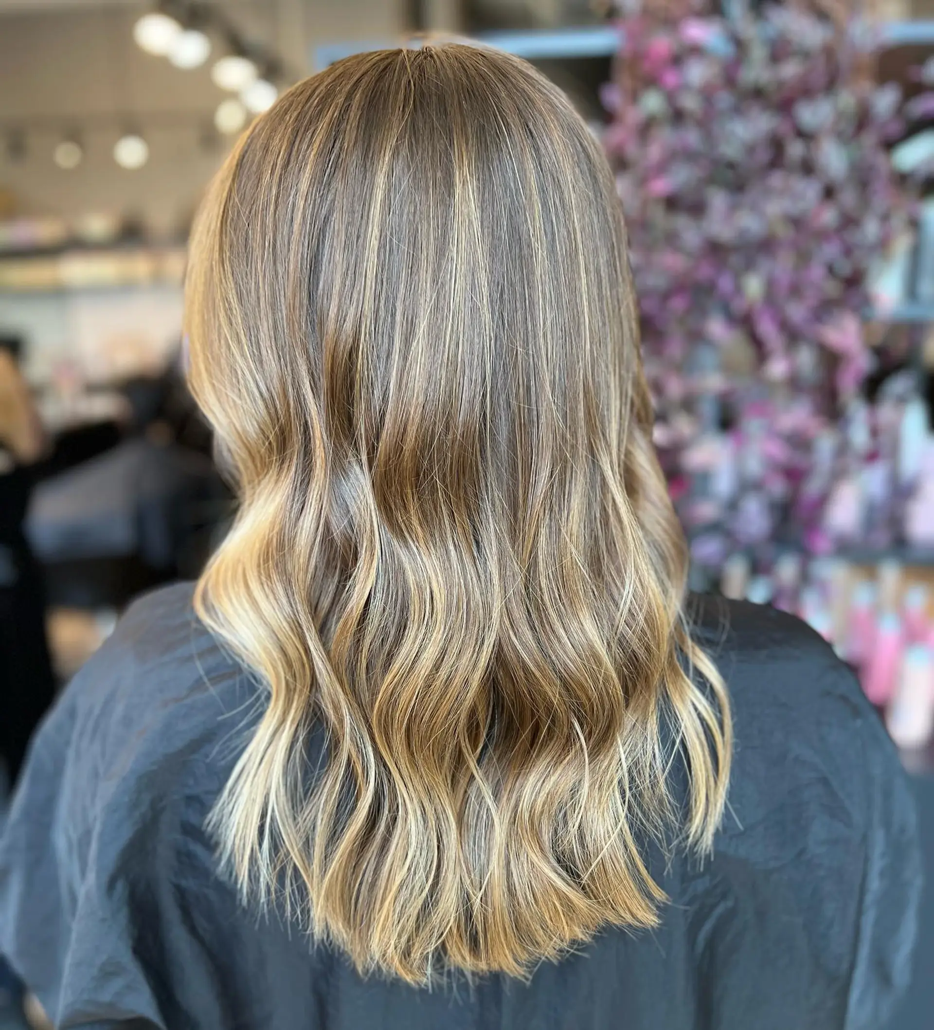 A medium-length hairstyle featuring a brown to honey blonde balayage with soft beachy waves. 1