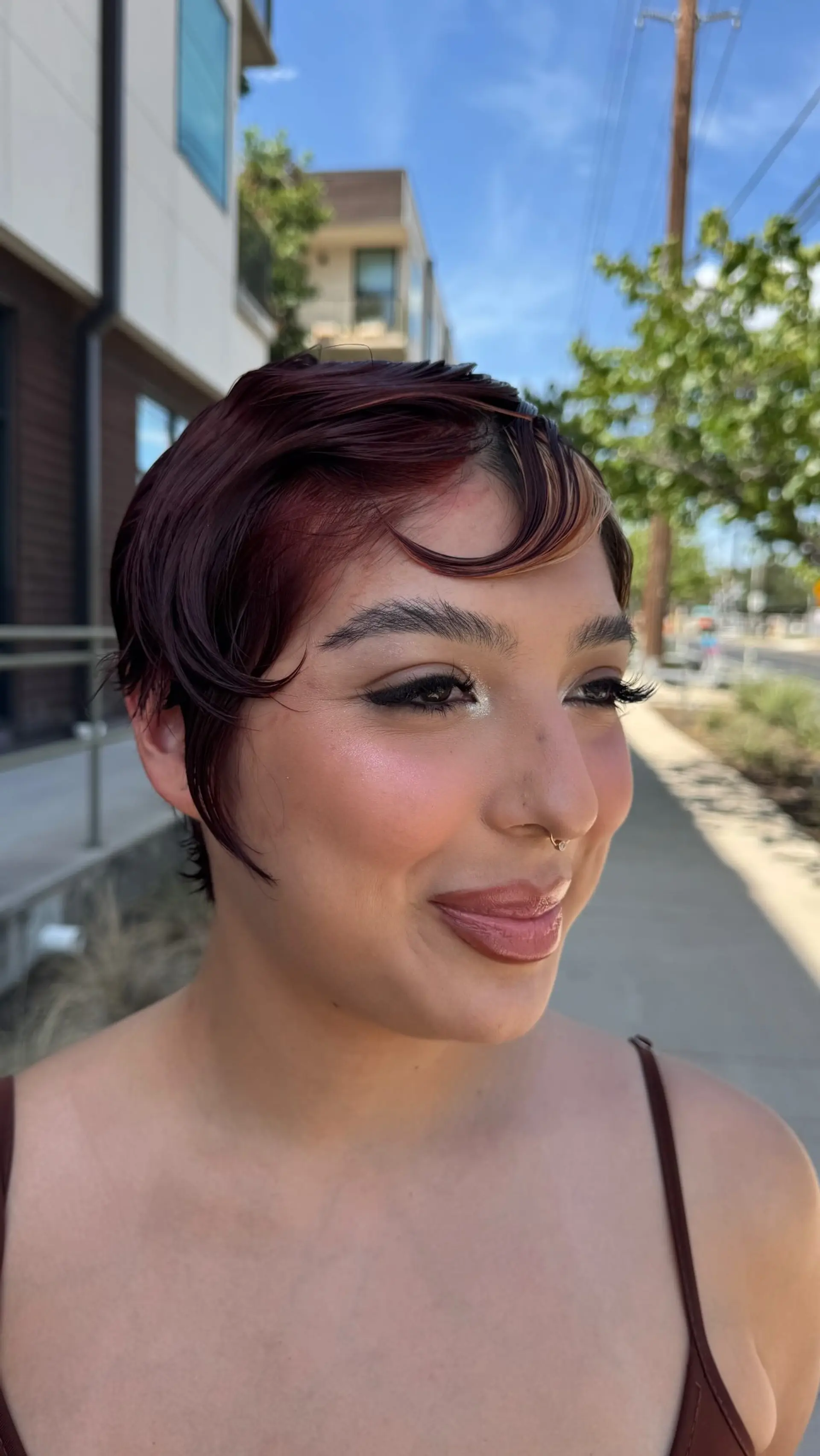 A short, sleek pixie cut in a rich reddish-burgundy tone styled with curved fringe and soft blonde accents. 1